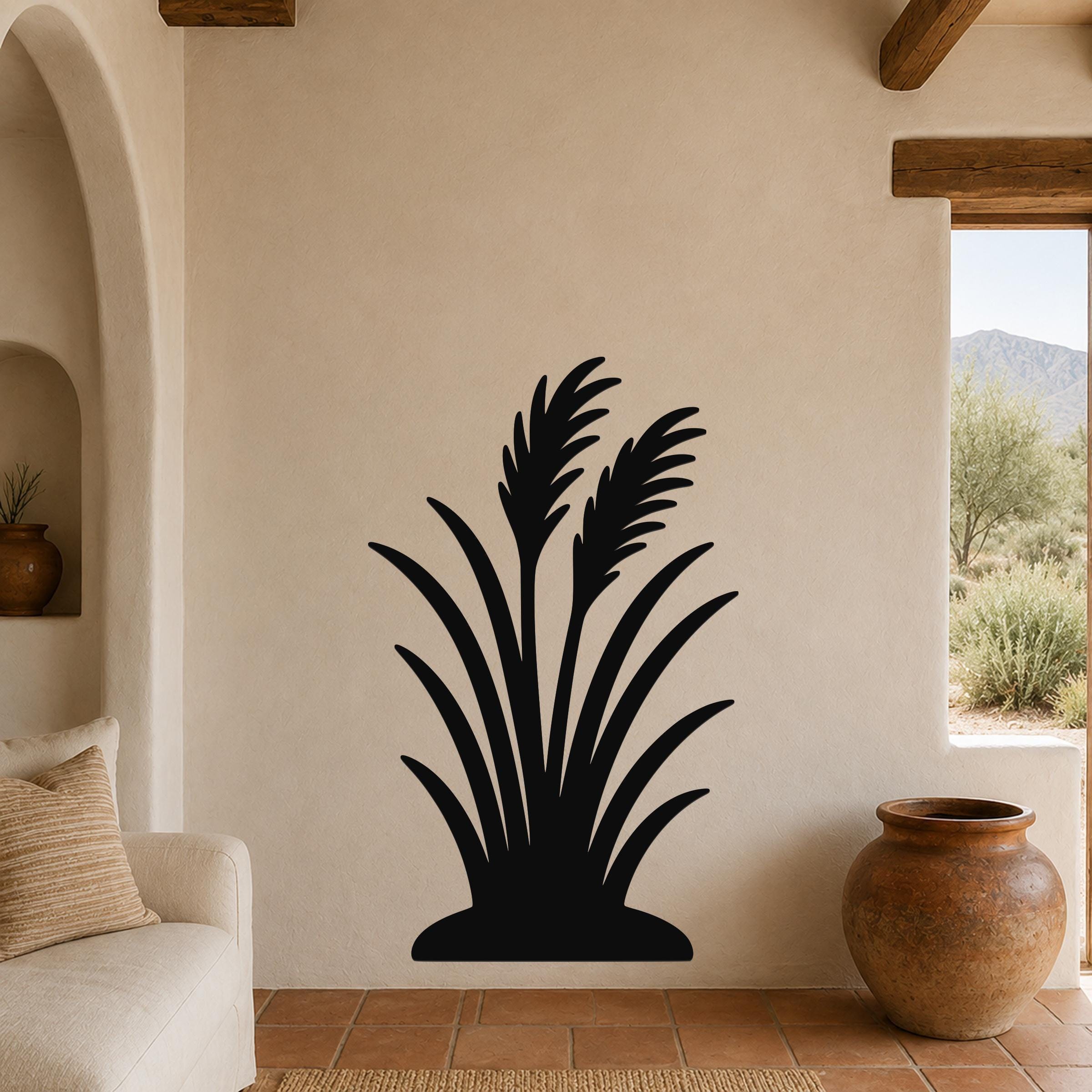 Black metal wall art in a wild grass silhouette design, mounted on a beige stucco wall in a living room with terracotta flooring and wooden beams.