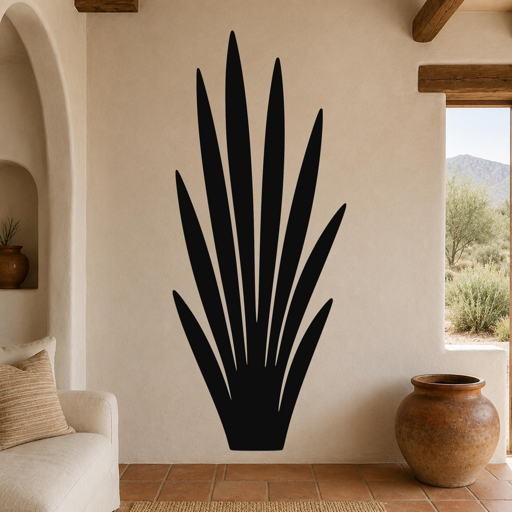 Black metal wall art in a tall, spiky agave silhouette, mounted on a textured beige wall above a terracotta-tiled floor in a living room.