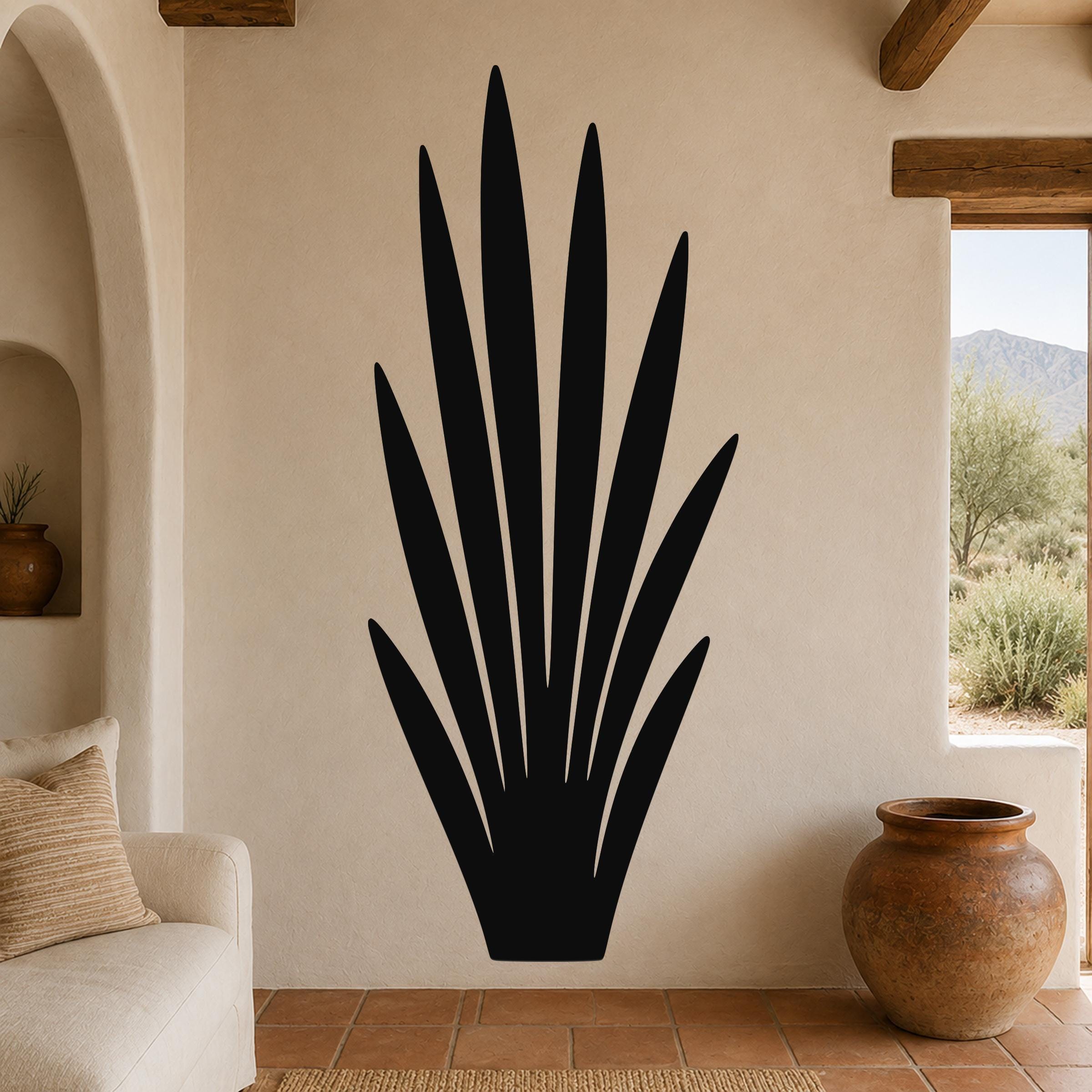 Black metal wall art in a tall, spiky agave silhouette, mounted on a textured beige wall above a terracotta-tiled floor in a living room.
