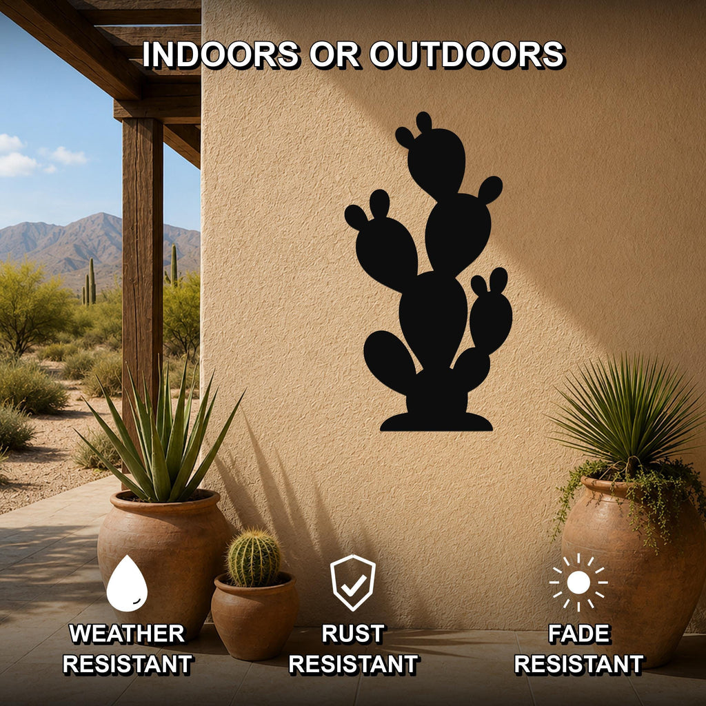 Black metal prickly pear cactus wall art silhouette mounted on a beige outdoor wall, displayed on a patio with potted plants and desert scenery in the background.