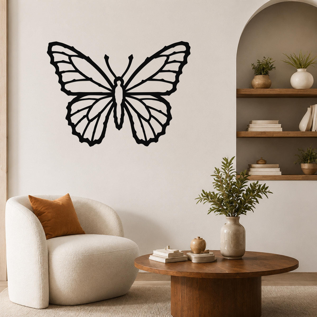 Black metal butterfly wall art with detailed wing cutouts, mounted on a living room wall above a round wooden coffee table.