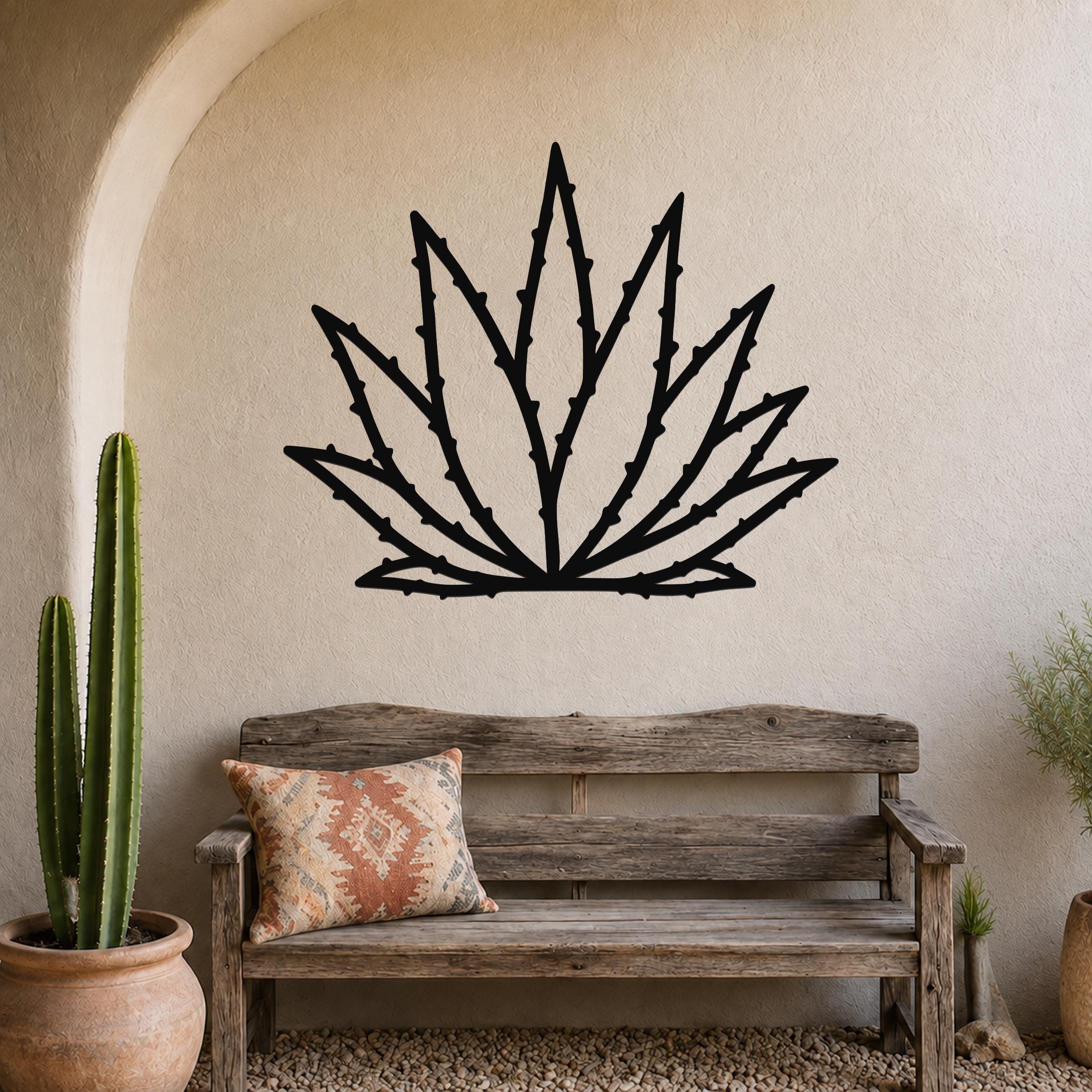 Black metal agave wall art with spiky leaf cutouts, mounted on a stucco wall above a wooden bench in a desert-style patio.