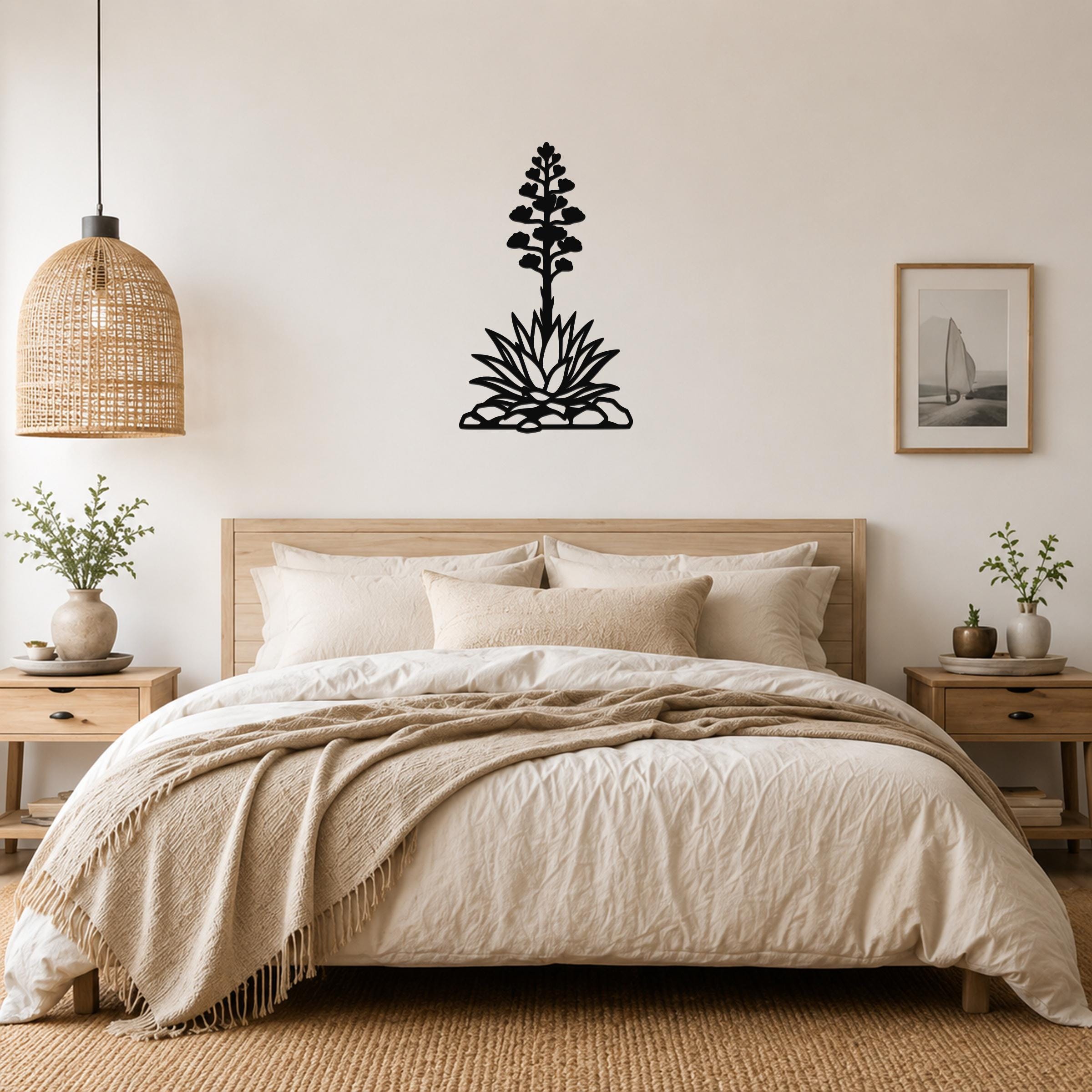 Black metal agave wall art with a blooming flower silhouette, mounted above a bed in a neutral bedroom.