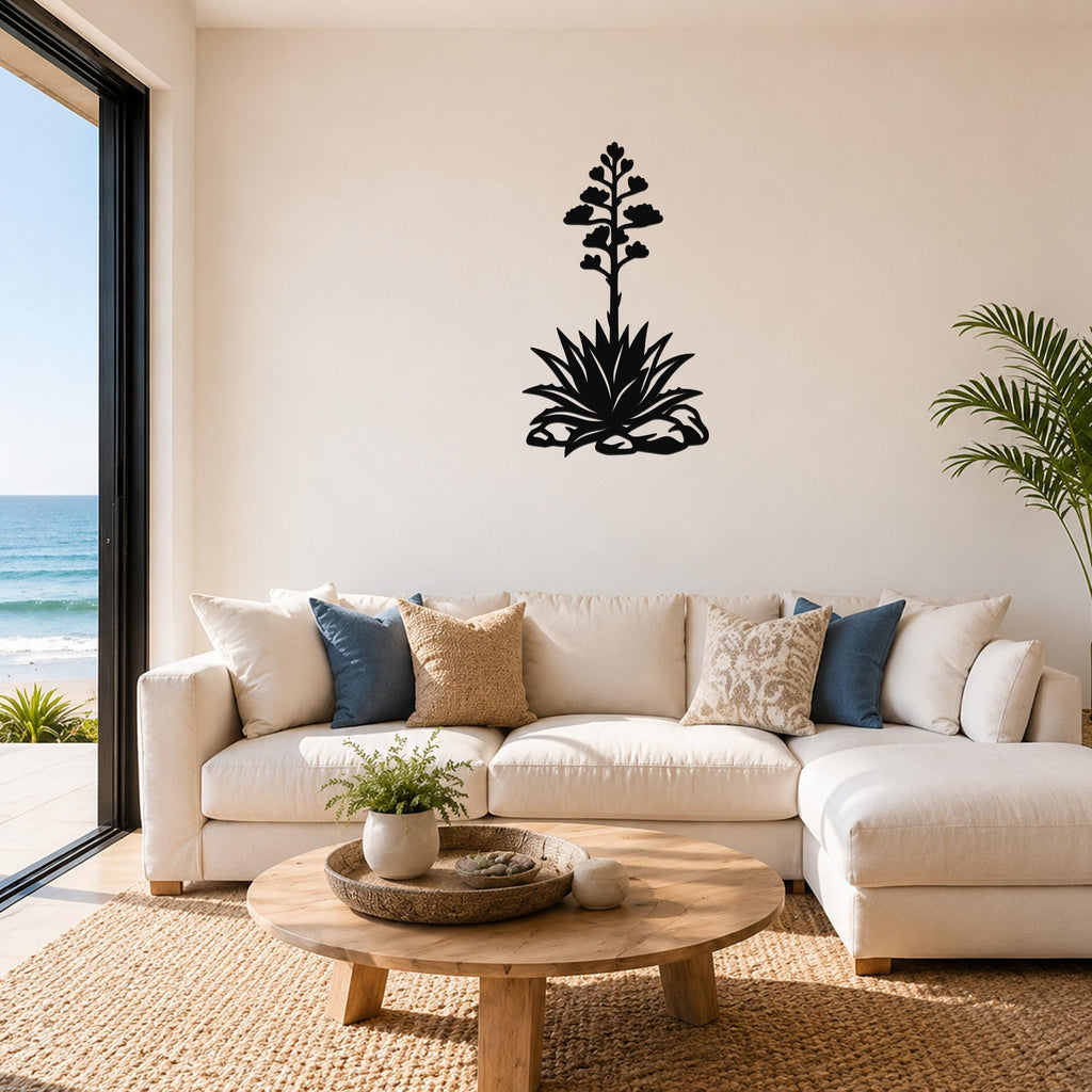Black metal agave wall art with a blooming flower silhouette, mounted above a white sofa in a living room with ocean views.