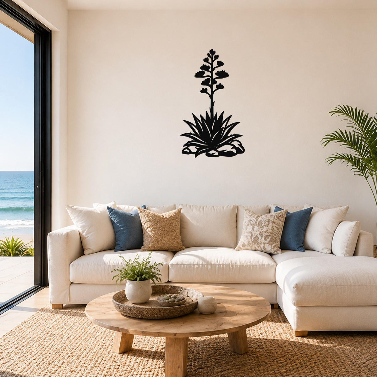 Black metal agave wall art with a blooming flower silhouette, mounted above a white sofa in a living room with ocean views.