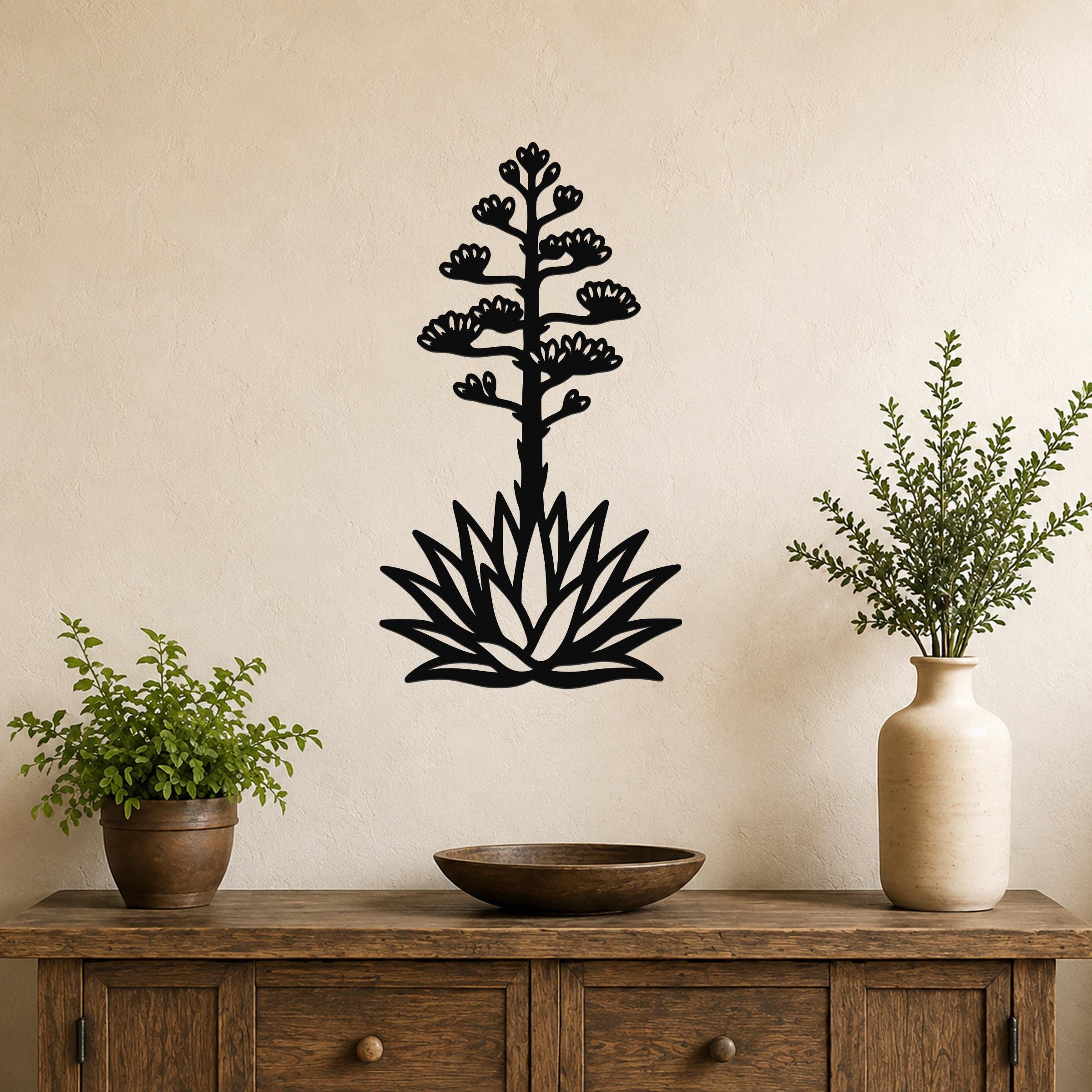 Black metal agave wall sculpture with blooming flower cutouts, mounted on a beige wall above a wooden console table.