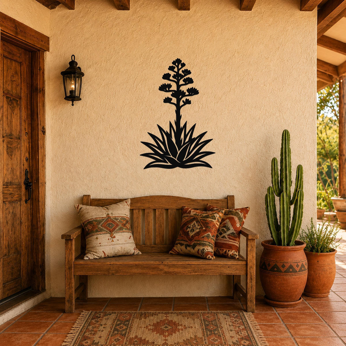 Black metal agave wall art with a blooming flower silhouette, mounted on a stucco wall above a wooden bench in a patio entryway.