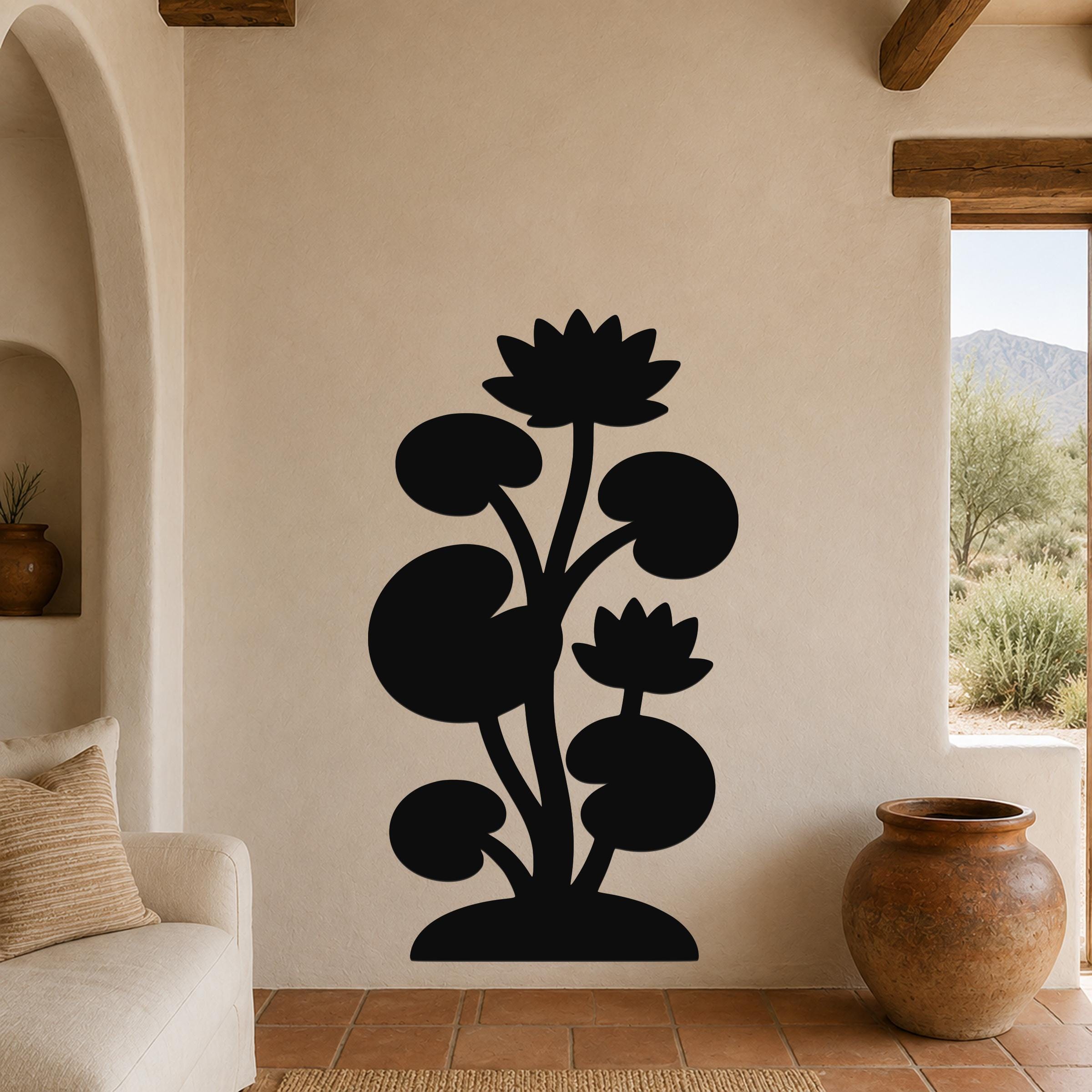 Black metal wall art silhouette of a lotus water lily plant with two flowers and round leaves, mounted on a beige wall in a living room with terracotta flooring.