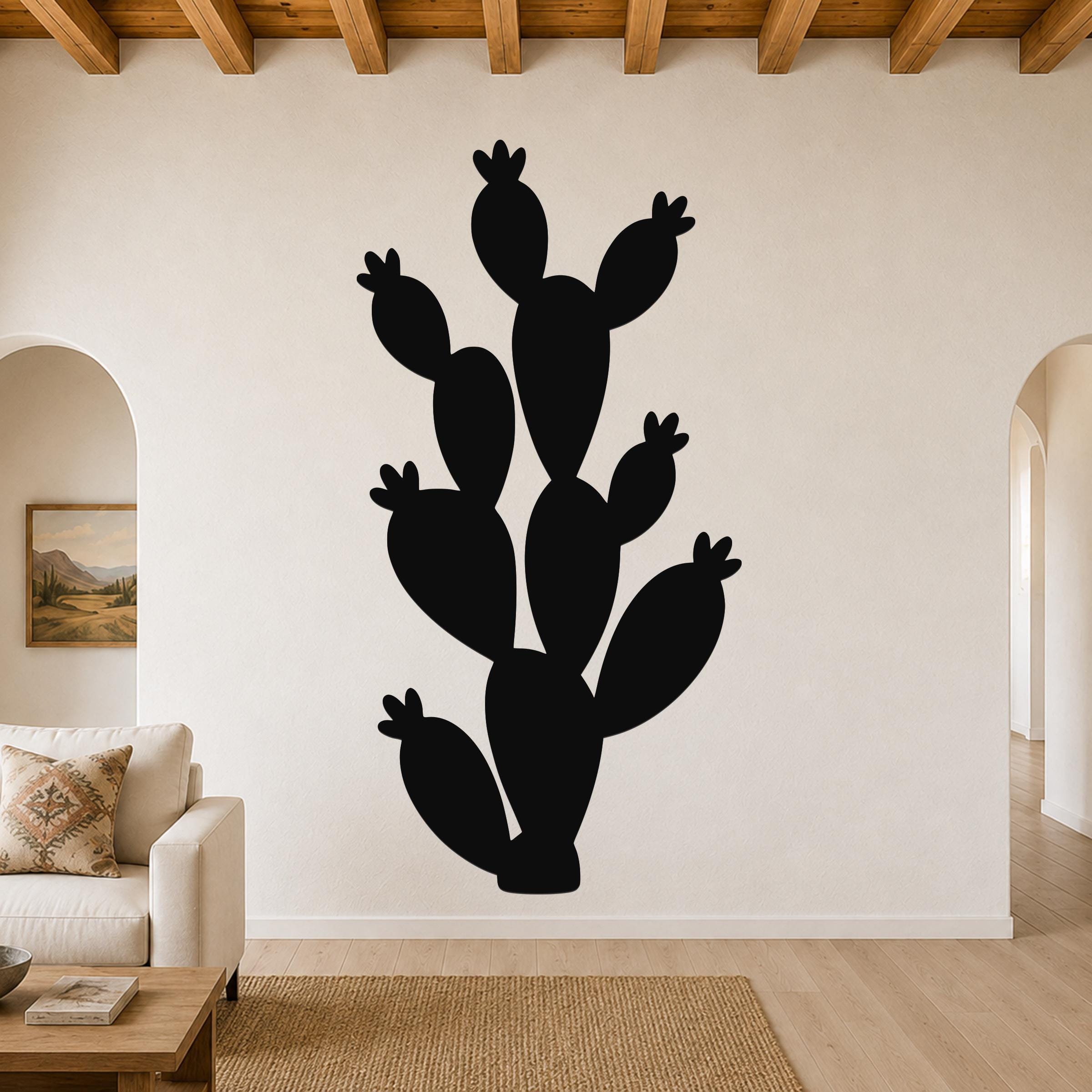 Black metal prickly pear cactus wall art with multiple segmented pads and small flower cutouts, mounted on a living room wall above a sofa.