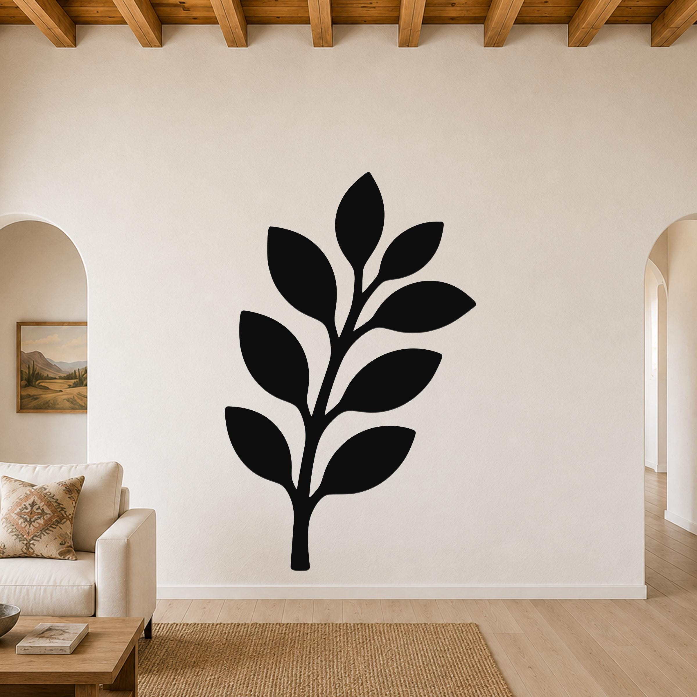 Black metal olive branch wall art with leaf cutouts, mounted on a living room wall above a sofa.