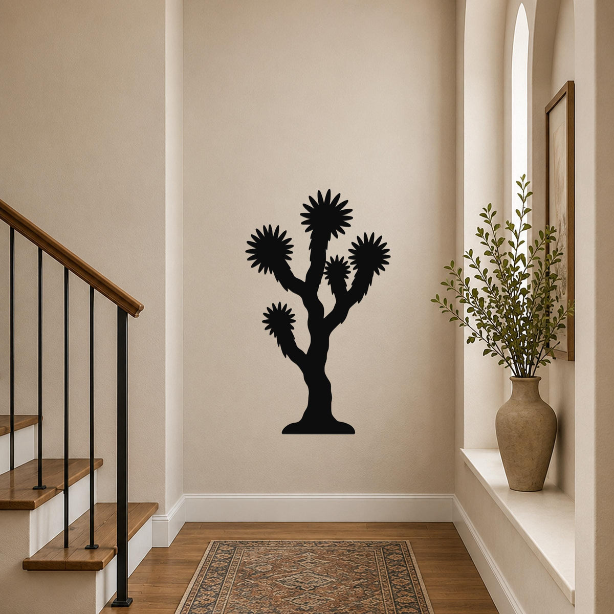 Black metal Joshua tree wall art with starburst-shaped branches, mounted on a beige hallway wall above a patterned rug near a staircase.