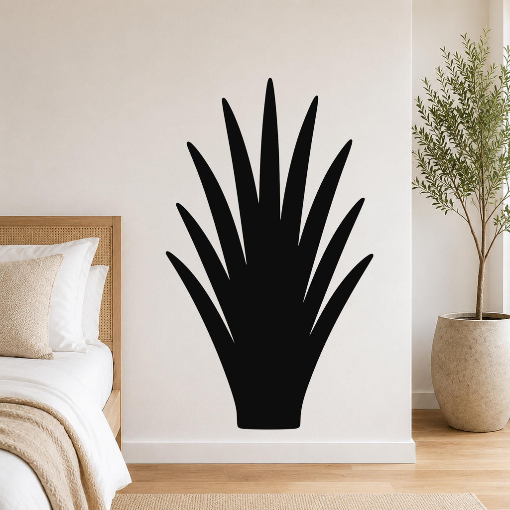 Black metal wall art in the silhouette of a spiky desert plant, mounted on a white wall above a bed in a bedroom.