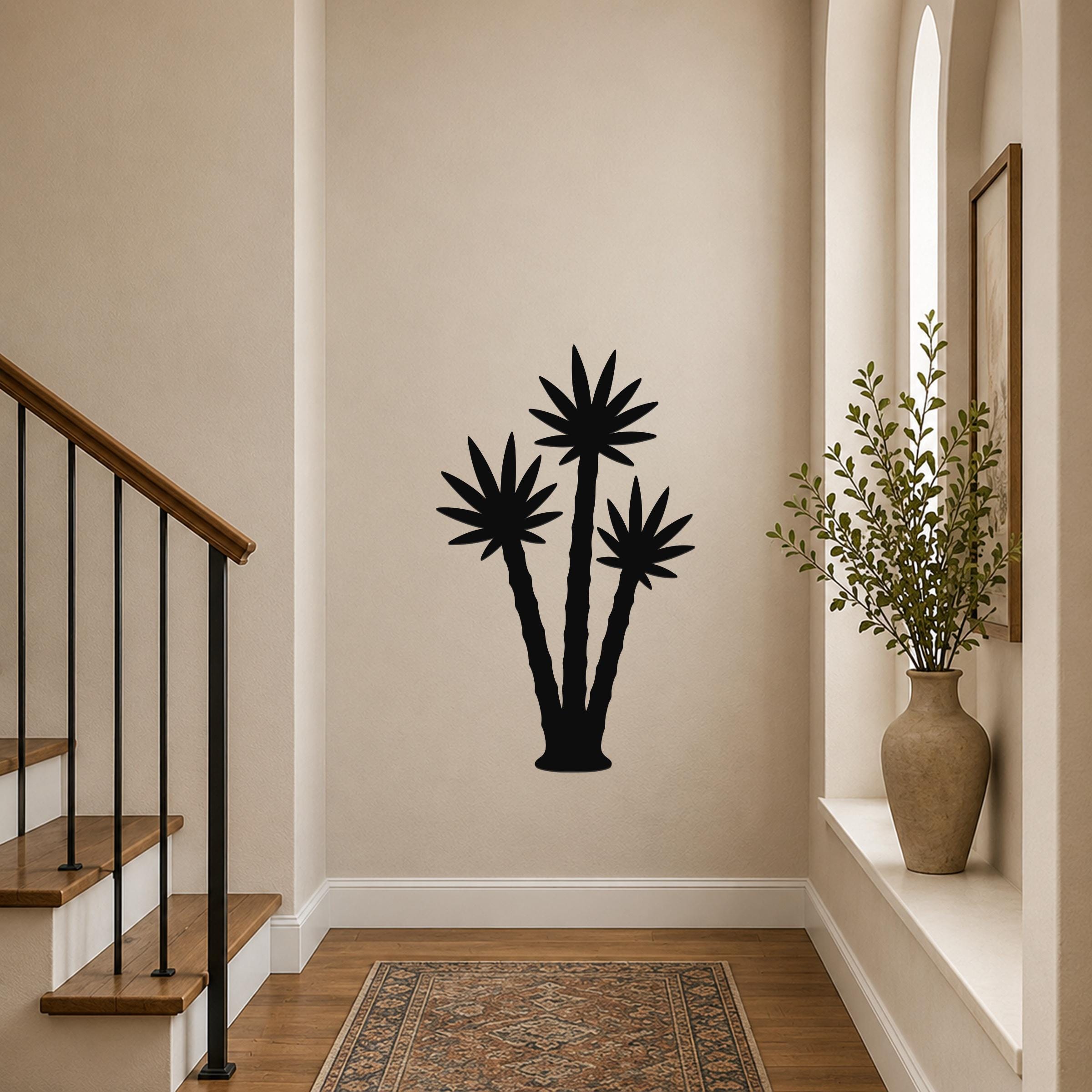 Black metal wall art featuring a silhouette of three palm trees, mounted on a hallway wall above a patterned rug near a staircase.
