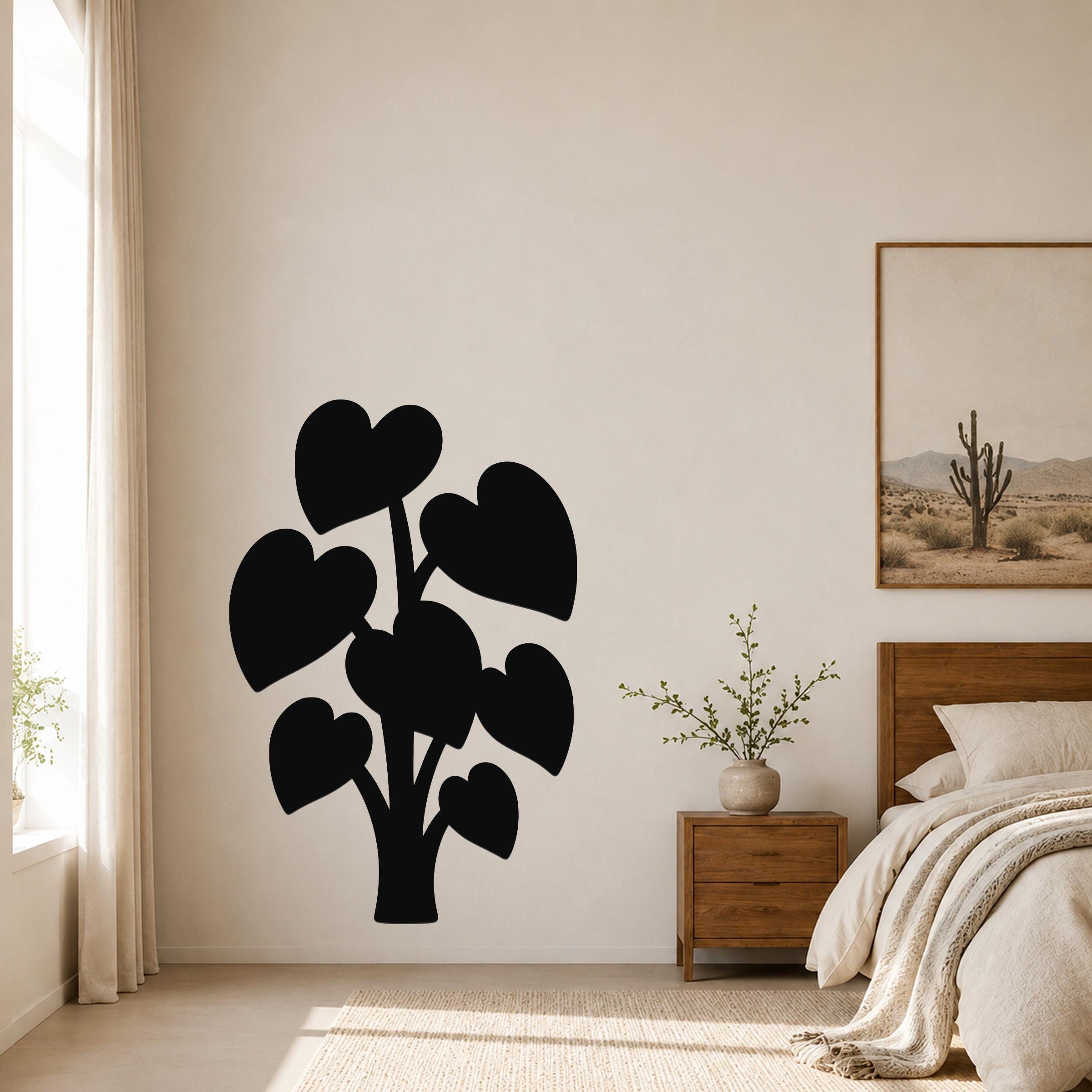 Black metal wall art in the silhouette of a plant with heart-shaped leaves, mounted on a bedroom wall above a nightstand.