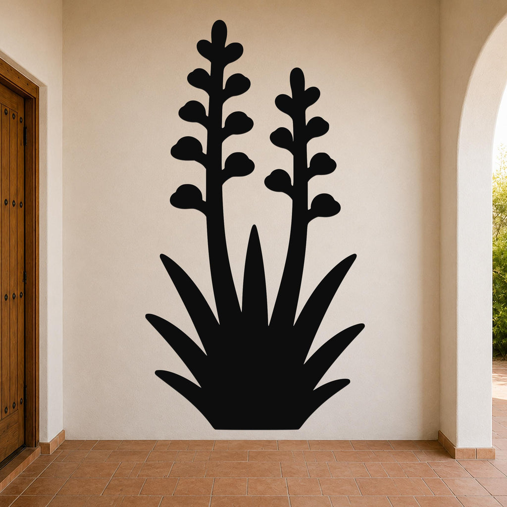 Black metal wall art in the silhouette of a blooming agave plant with two tall stems and spiky leaves, mounted on a beige wall in a covered entryway.