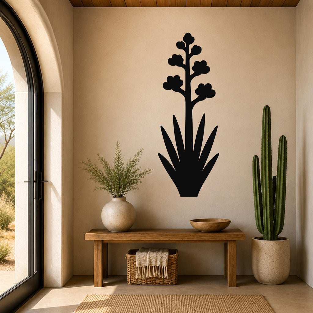 Black metal agave wall art with blooming flower silhouette, mounted on a beige wall above a wooden bench in a sunlit entryway.