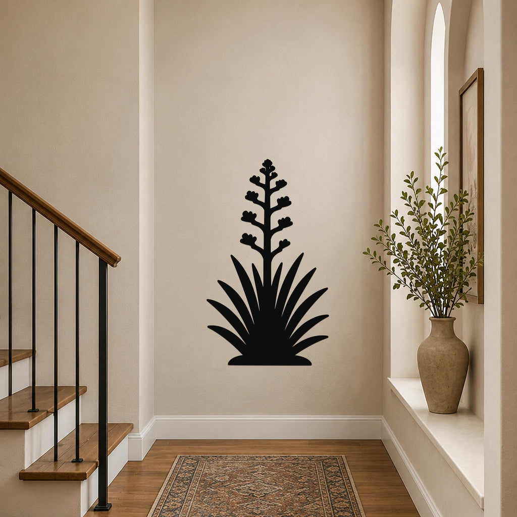 Black metal wall art silhouette of a blooming agave plant with a tall flower stalk and spiky leaves, mounted on a hallway wall above a patterned rug.