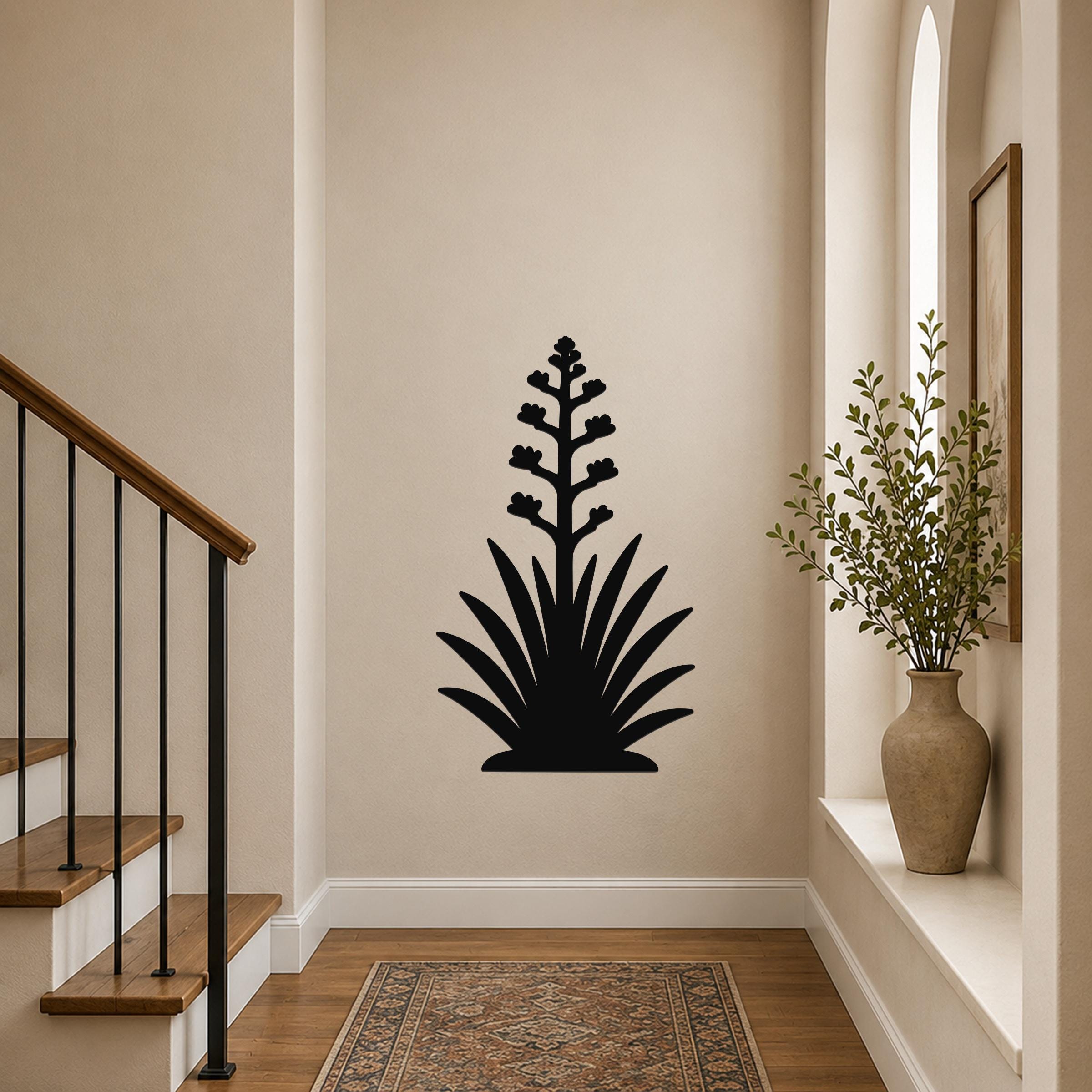 Black metal wall art silhouette of a blooming agave plant with a tall flower stalk and spiky leaves, mounted on a hallway wall above a patterned rug.