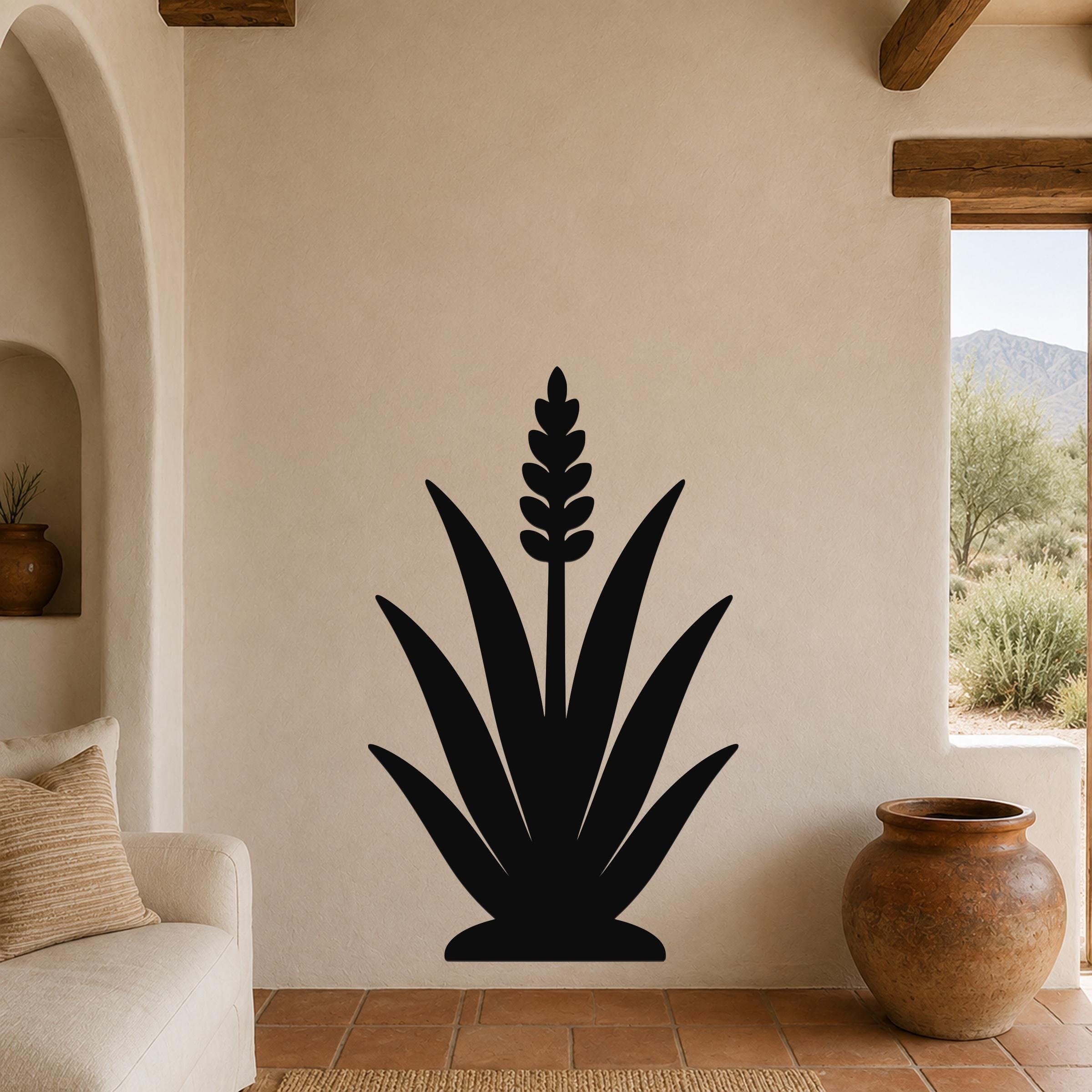 Black metal agave wall art with a central flower spike cutout, mounted on a beige living room wall above a sofa.