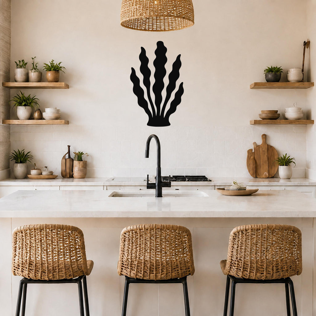 Black metal kelp wall art with wavy frond cutouts, mounted on a kitchen wall above a counter with open shelves and woven bar stools.