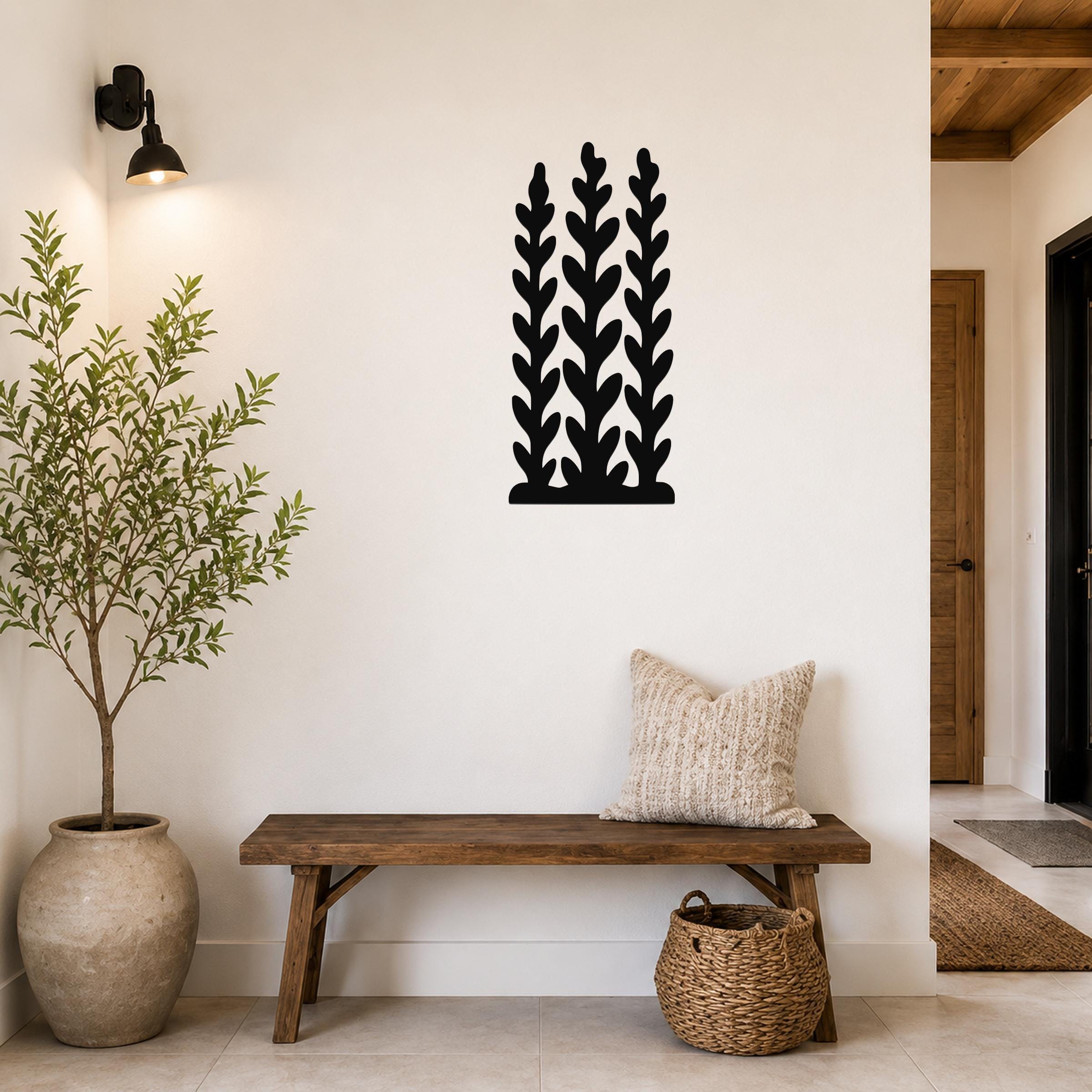 Black metal wall art with a kelp and seaweed silhouette design, mounted on a white wall above a wooden bench in a entryway.