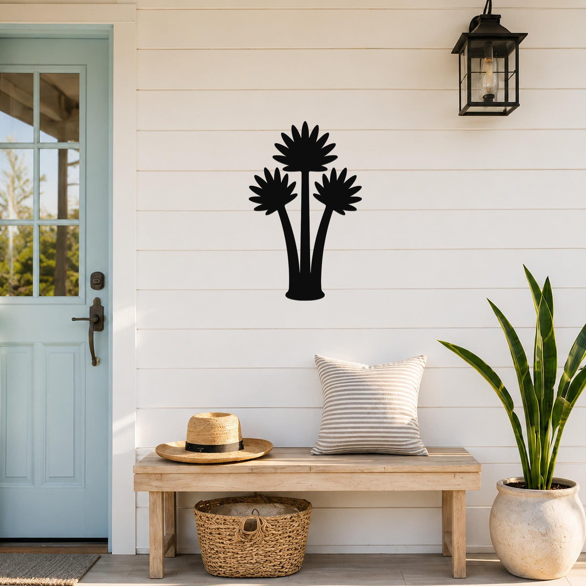 Black metal fan palm tree wall art with three distinct frond silhouettes, mounted on a white shiplap wall above a wooden bench in a coastal entryway.