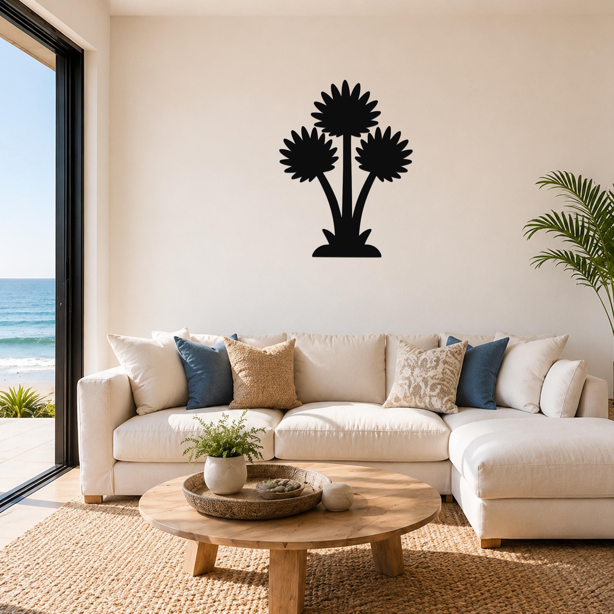 Black metal wall art with a silhouette of three palm trees, mounted above a white sofa in a living room with ocean views.
