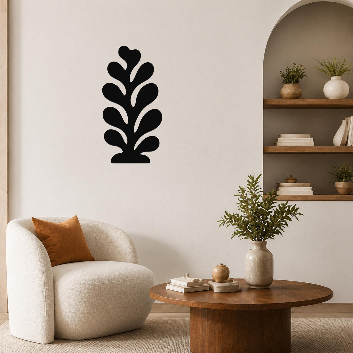 Black metal leaf wall art with layered cutout design, mounted on a living room wall above a round wooden coffee table.