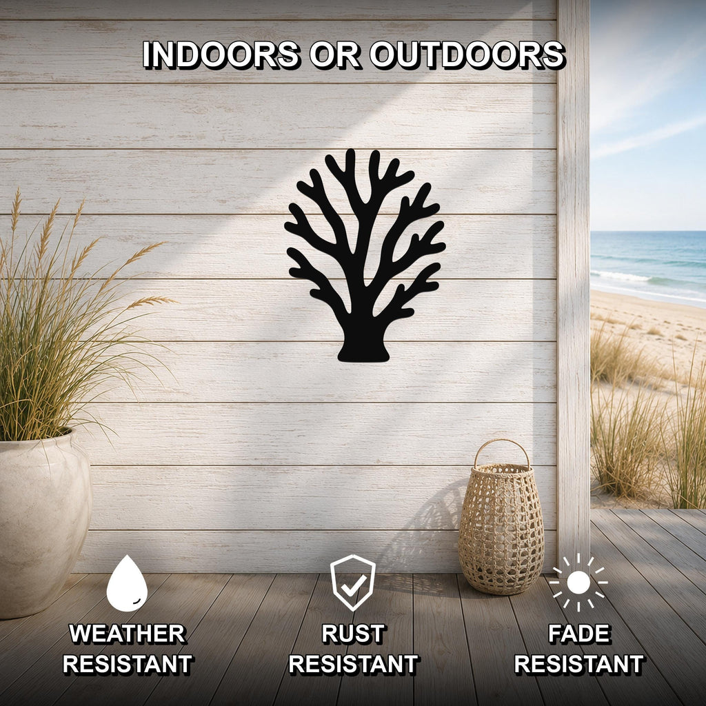 Black metal branching coral wall art with intricate cutout details, mounted on a light wood plank wall in an outdoor patio setting with a beach view.