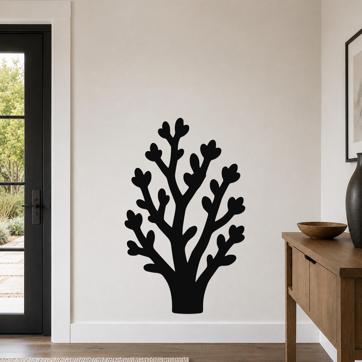 Black metal wall art in a tree silhouette with branching cutouts, mounted on a white wall in a living room near a door and console table.