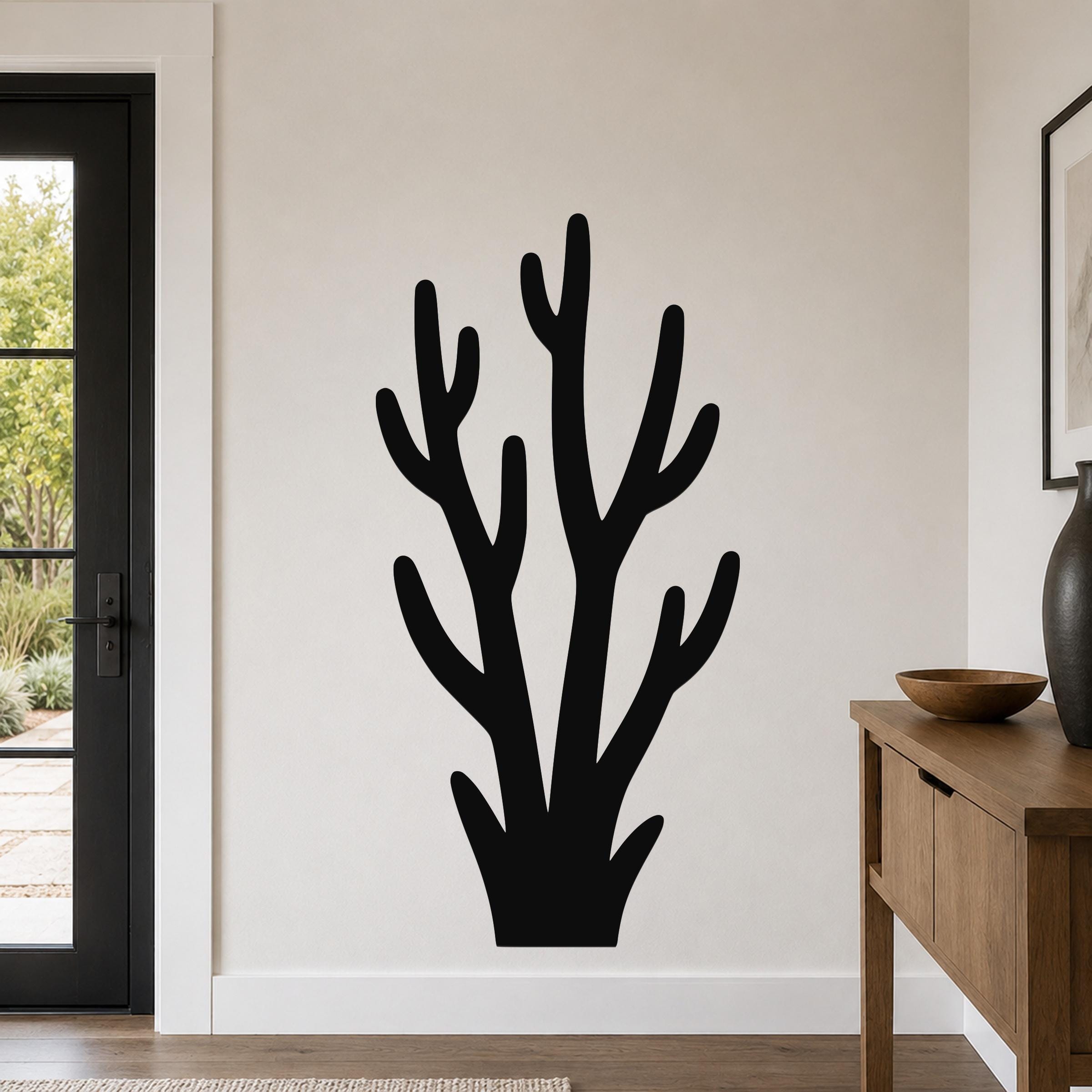 Black metal wall art in a coral or branch silhouette design, mounted on a light-colored wall above a wooden console table in a modern entryway.