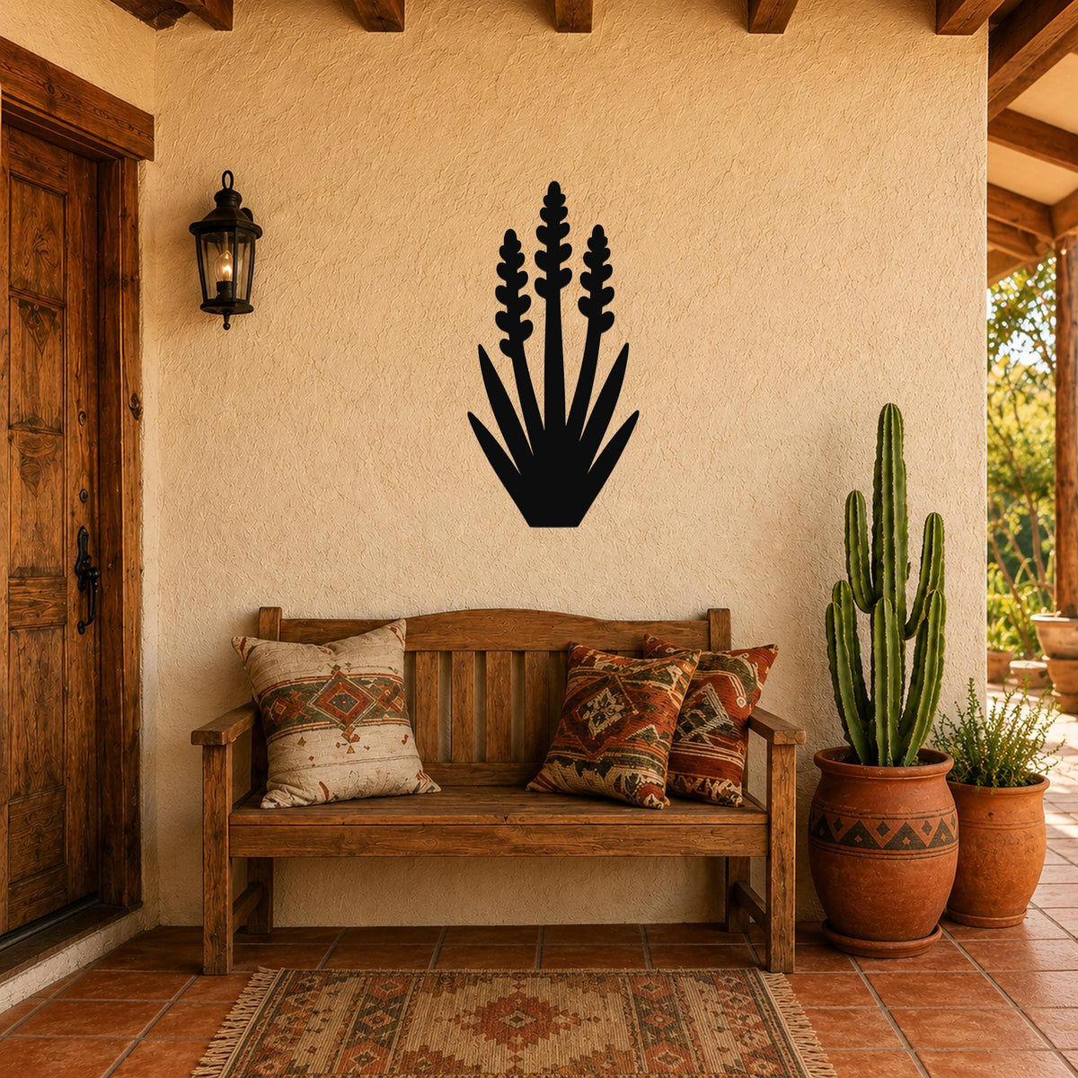 Black metal yucca wall art with layered leaf and bloom cutouts, mounted on a stucco wall above a wooden bench in a patio entryway.