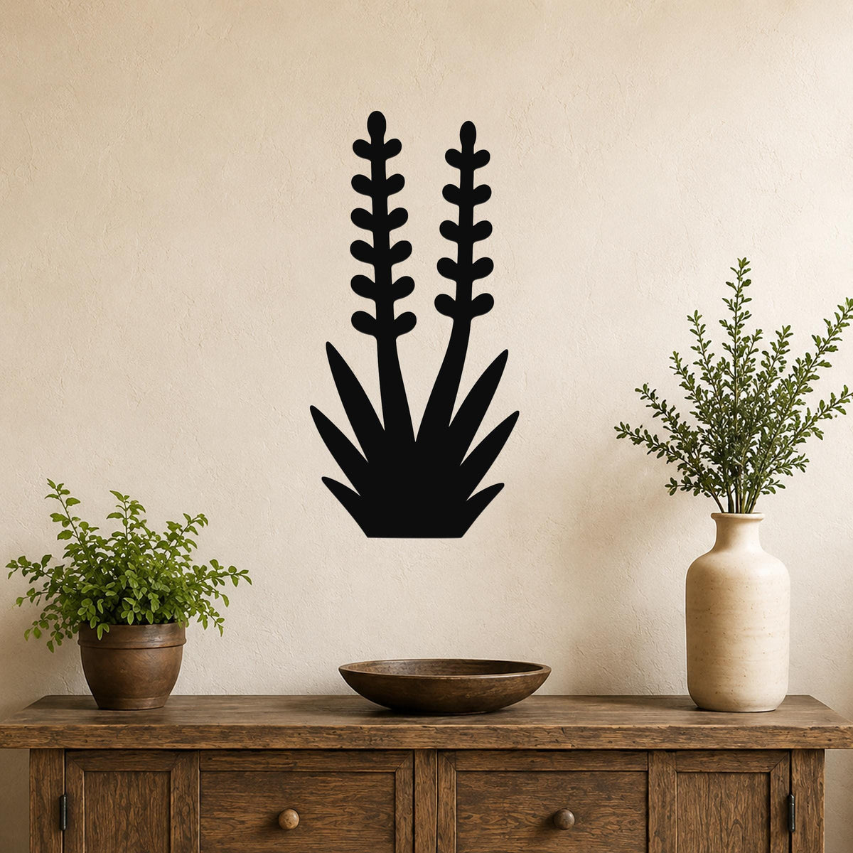 Black metal wall art in a yucca plant silhouette with two tall stems and spiky leaves, mounted on a beige wall above a wooden console table.