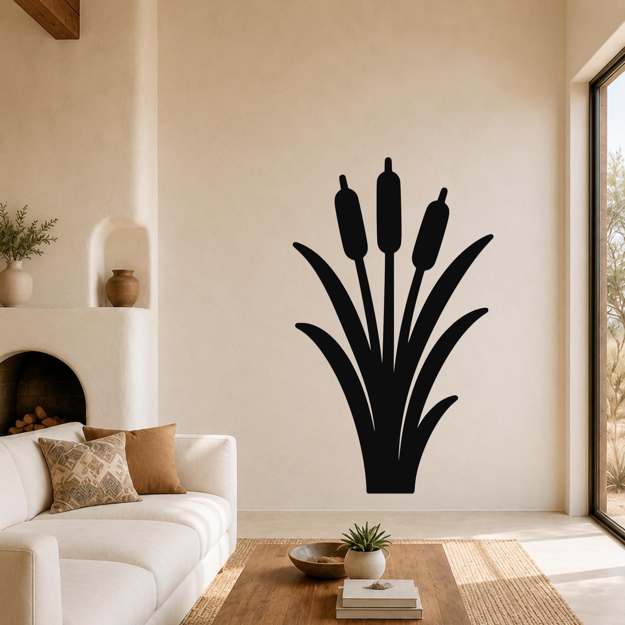 Black metal wall art silhouette of cattails with three seed heads and long leaves, mounted on a living room wall above a sofa.