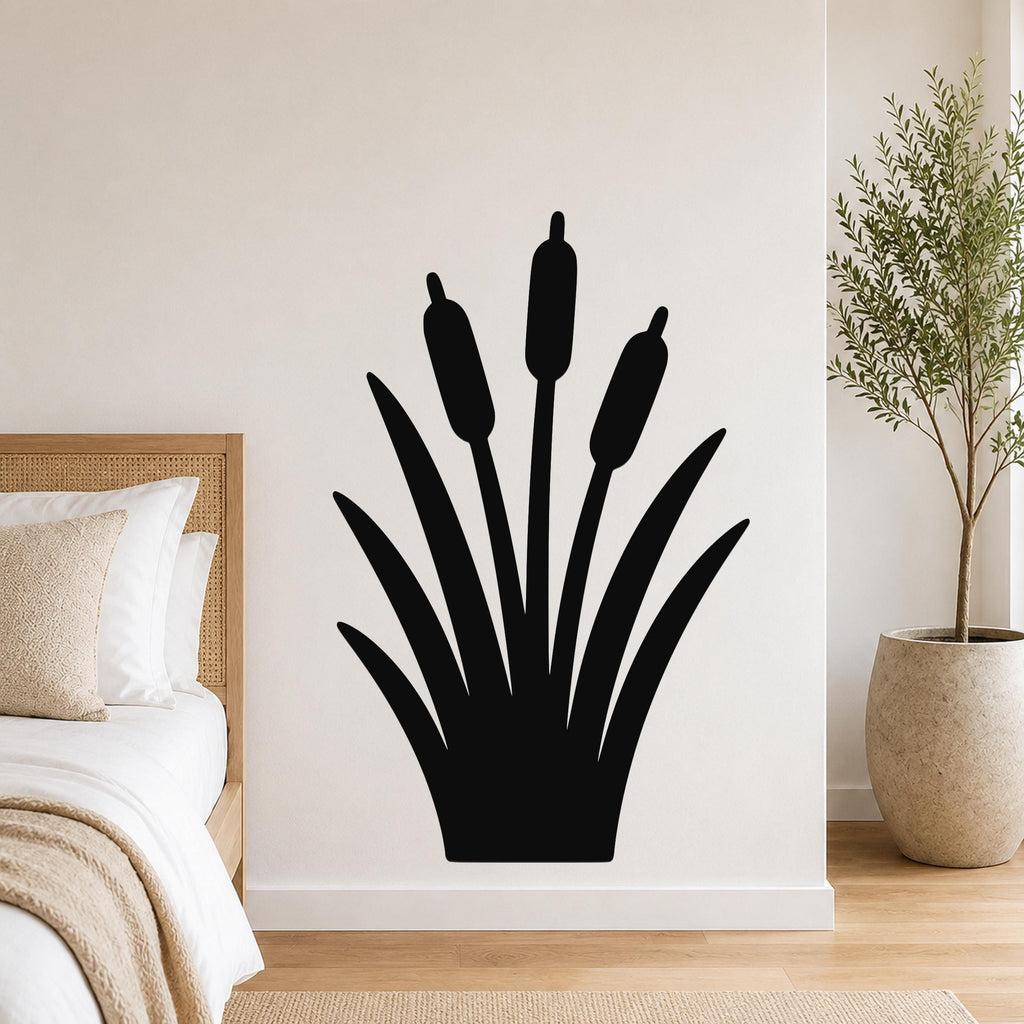 Black metal cattail wall art silhouette with three seed heads and long leaves, mounted on a white wall above a bed in a bedroom.