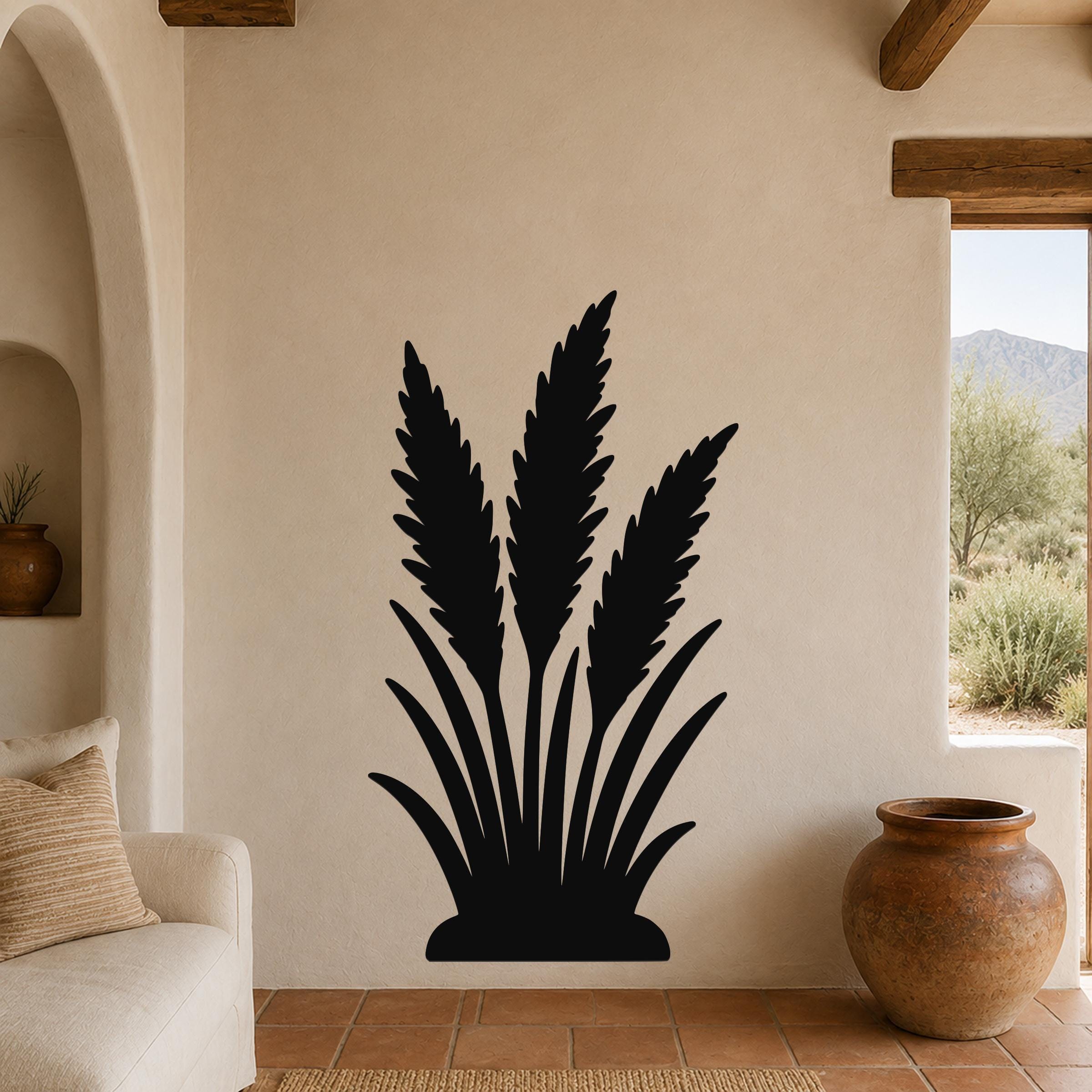 Black metal wall art in a silhouette of wild grass, mounted on a beige stucco wall in a living room with terracotta flooring and wooden beams.