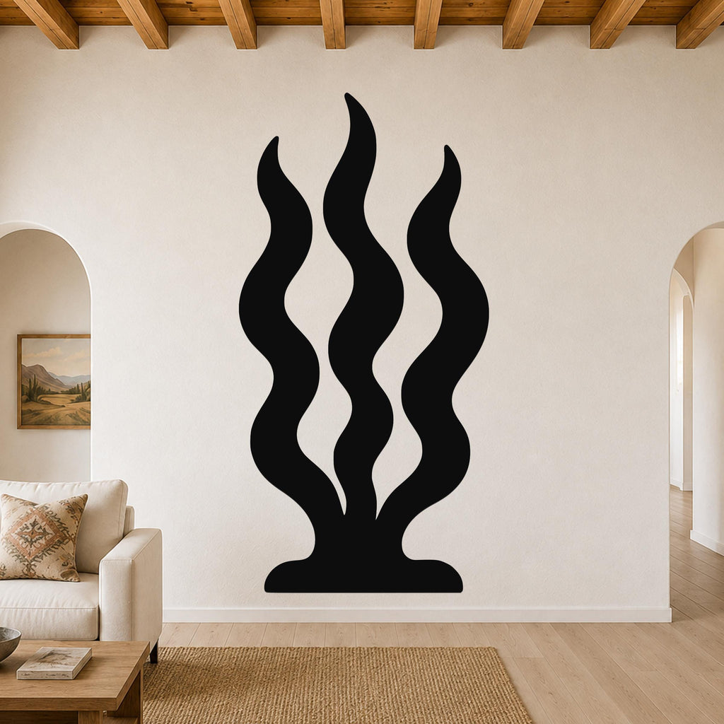 Black metal wall art with three wavy vertical cutouts resembling grass or seaweed, mounted on a living room wall above a sofa.