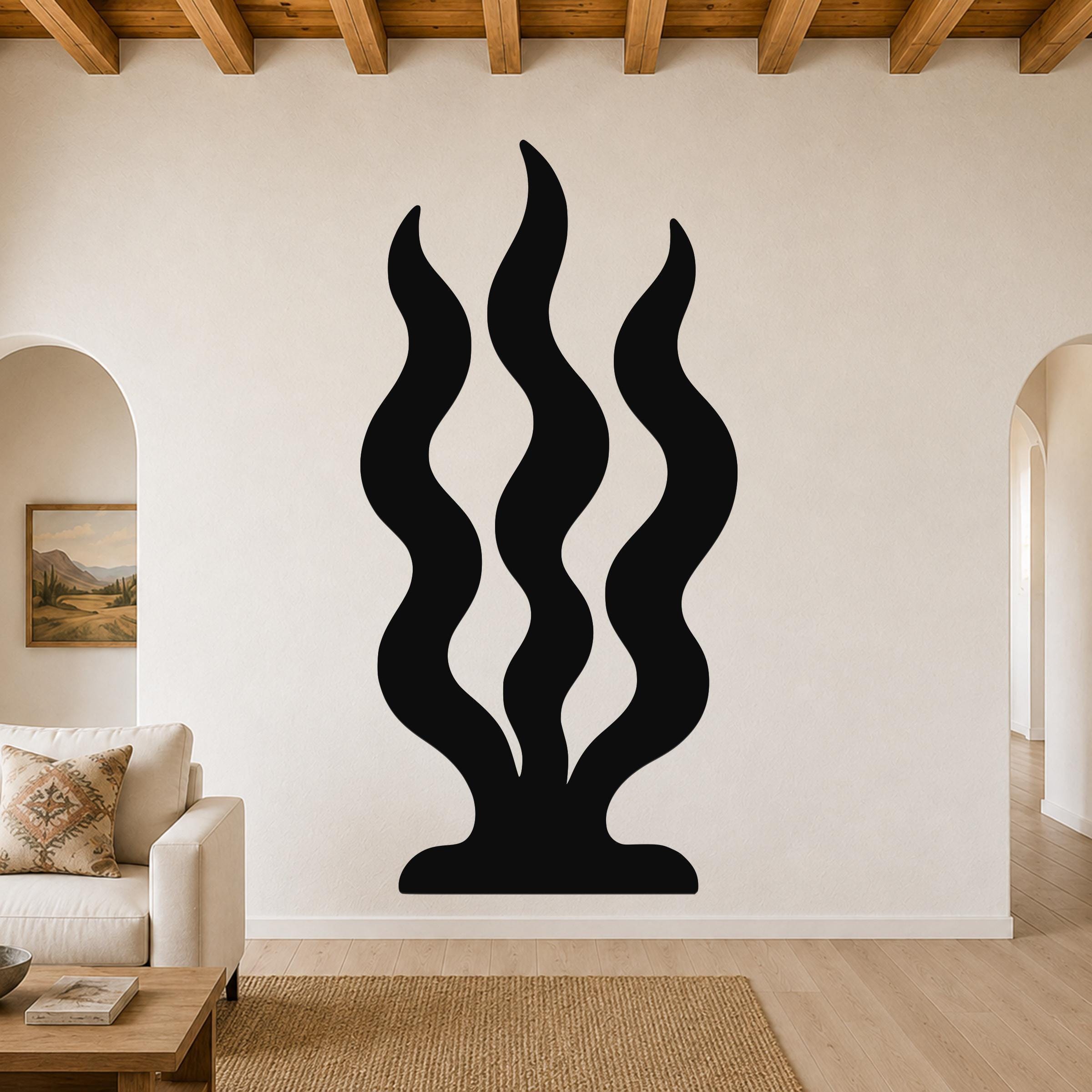 Black metal wall art with three wavy vertical cutouts resembling grass or seaweed, mounted on a living room wall above a sofa.