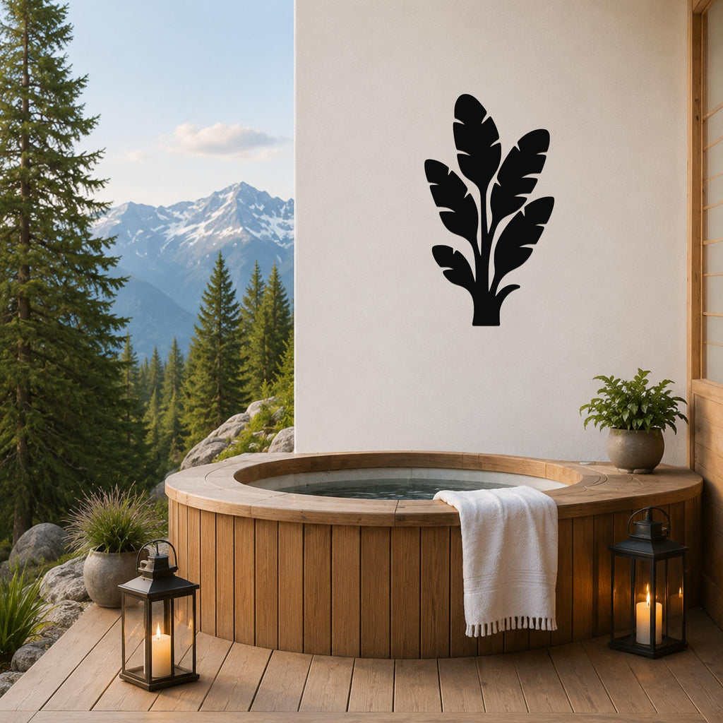 Black metal tropical leaves wall art silhouette mounted on a white wall above a wooden hot tub on a patio with mountain views.