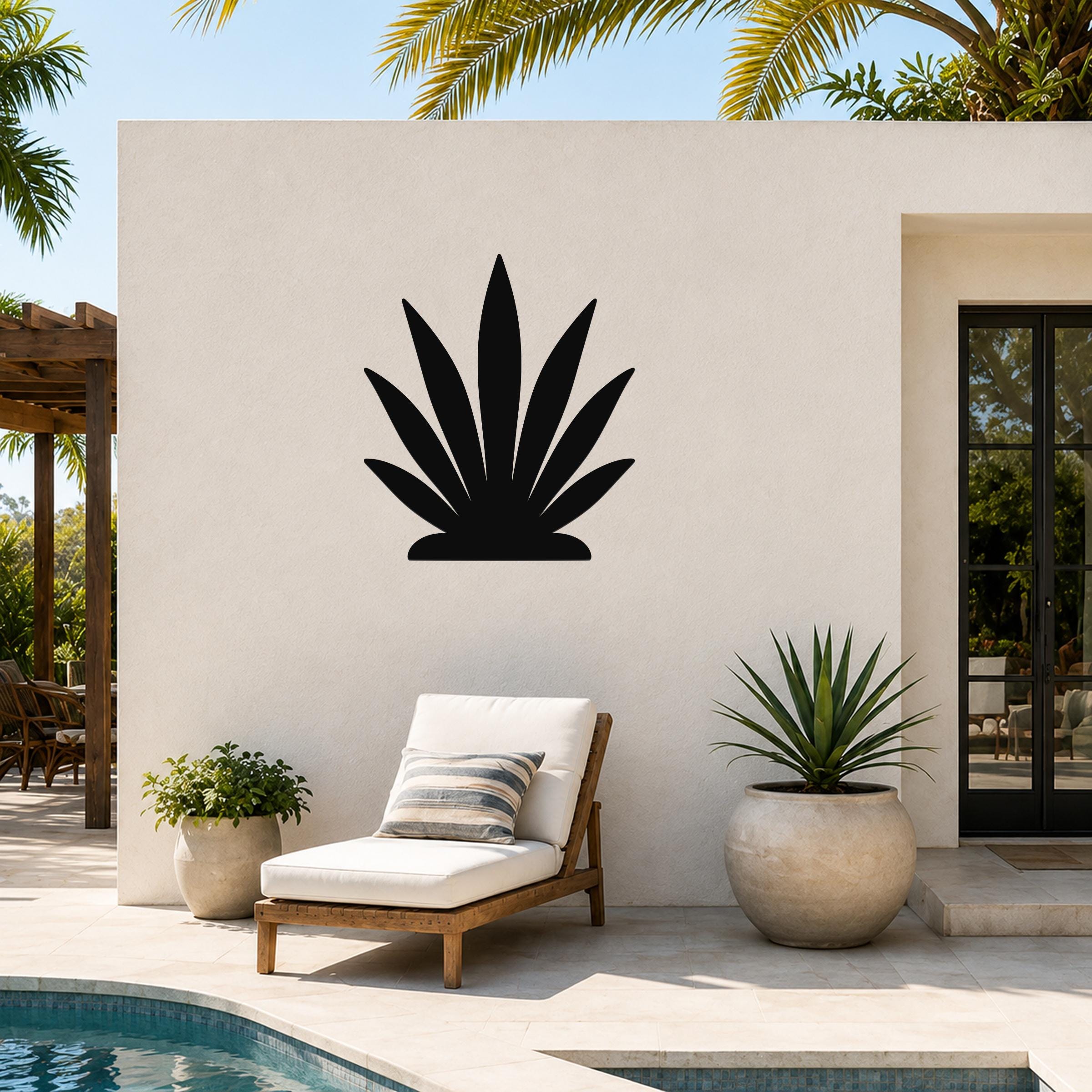 Black metal agave wall art silhouette mounted on a white outdoor wall above a lounge chair on a patio.