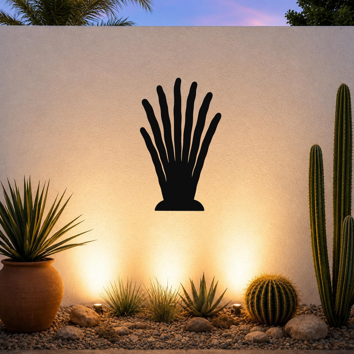 Black metal wall art in a hand-shaped silhouette with elongated fingers, mounted on an outdoor wall above a desert garden with cacti and warm uplighting.