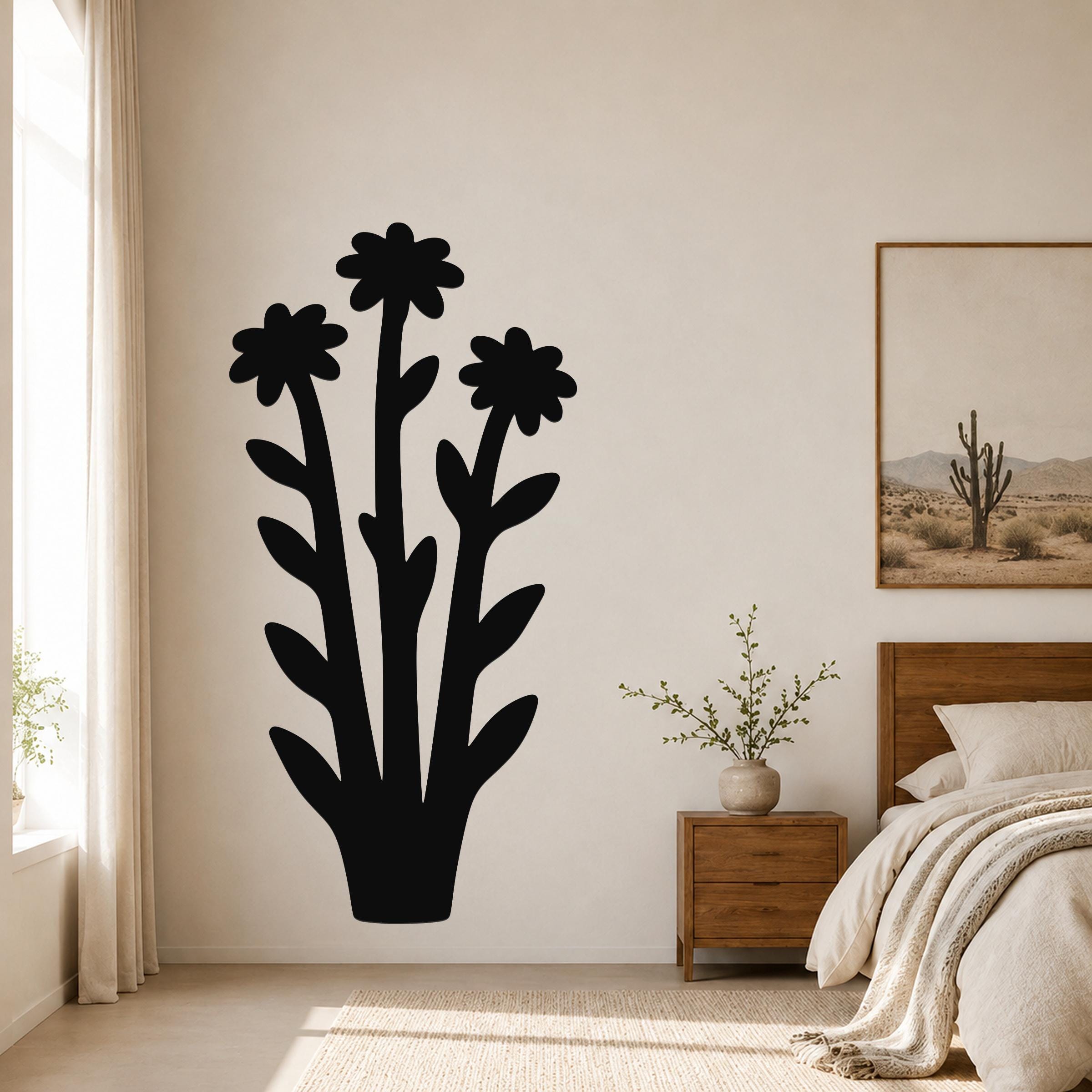 Black metal wall art in a silhouette of three wildflowers with leafy stems, mounted on a bedroom wall above a nightstand.