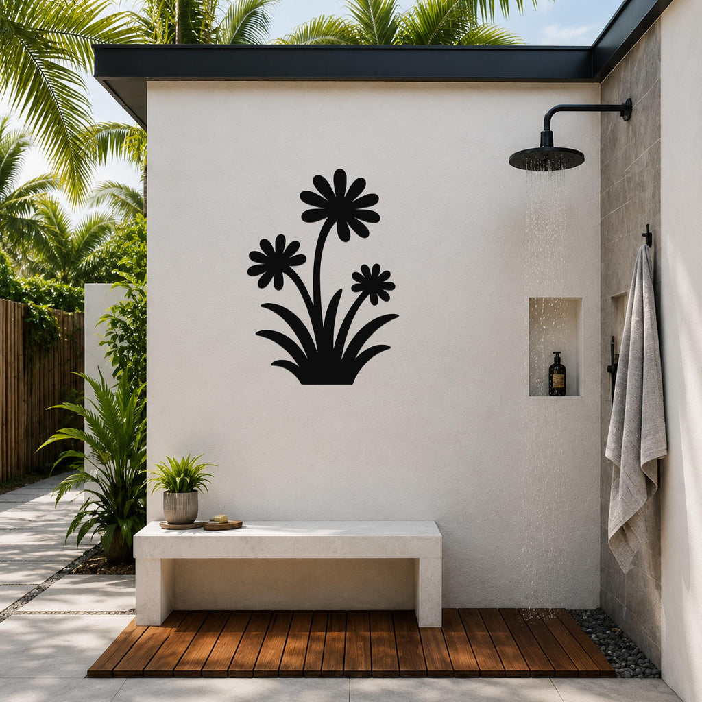 Black metal wildflower wall art with three daisy cutouts, mounted on a white outdoor shower wall above a concrete bench.