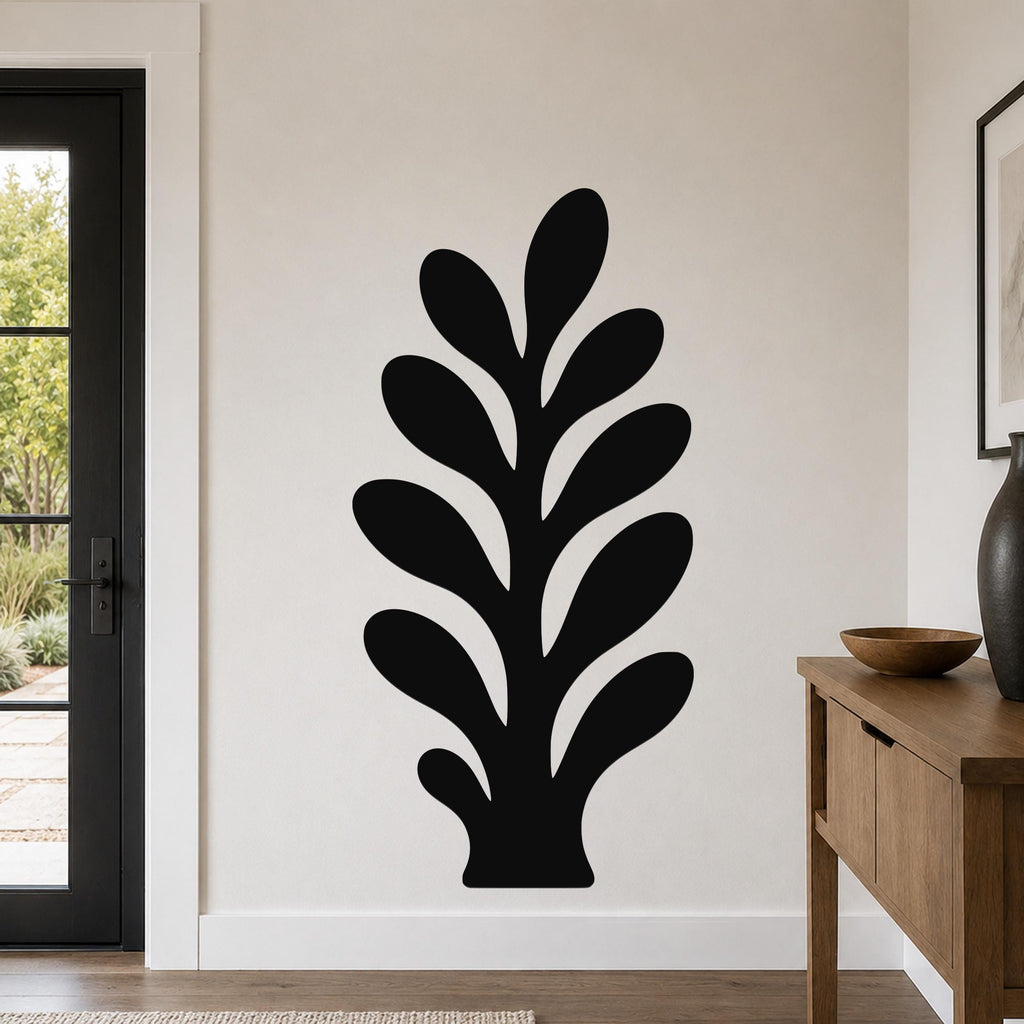 Black metal wall art in a leafy sprig silhouette with internal cutouts, mounted on a light-colored wall in a modern entryway.