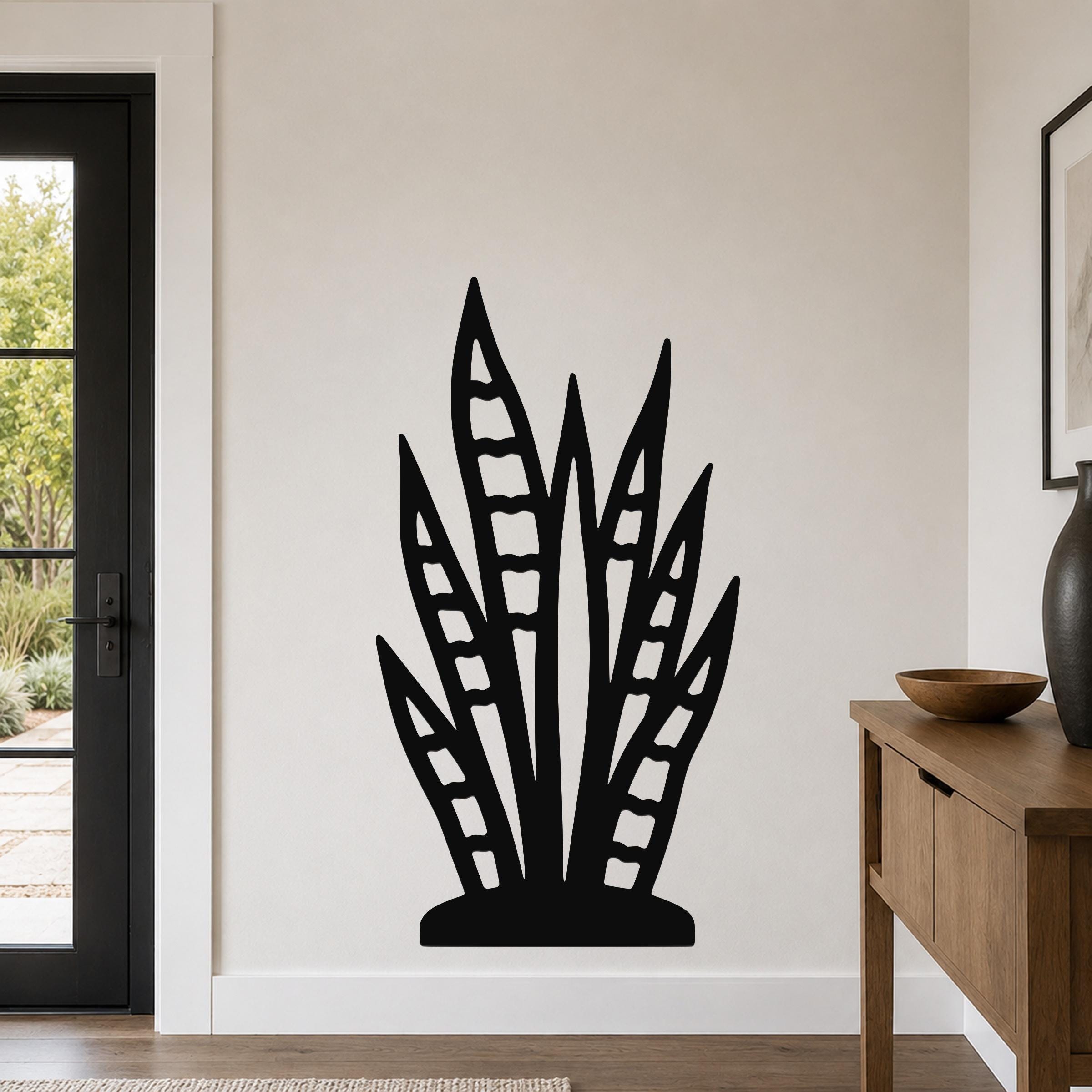 Black metal snake plant wall art with leaf cutouts, mounted on a living room wall above a wooden console table.