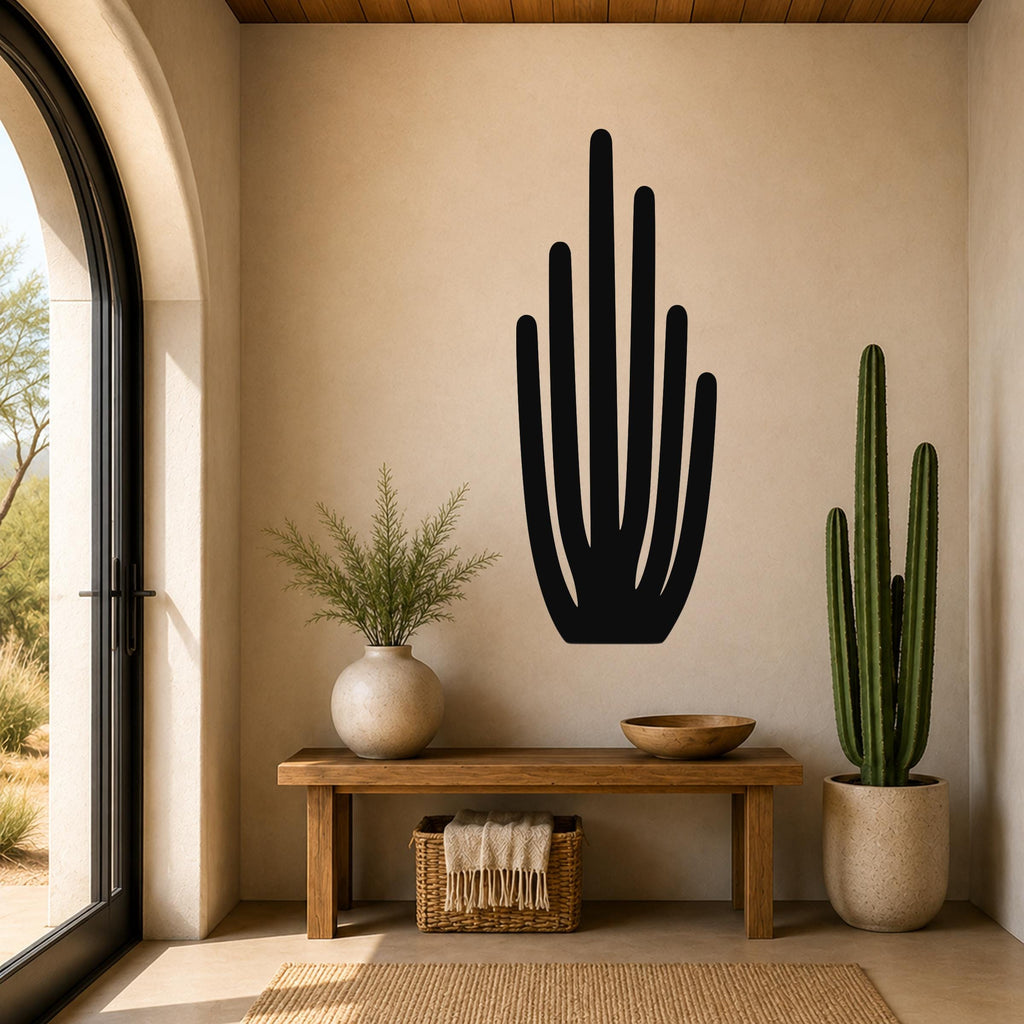 Black metal wall art in the silhouette of an organ pipe cactus, mounted on a beige wall above a wooden bench in a sunlit entryway.