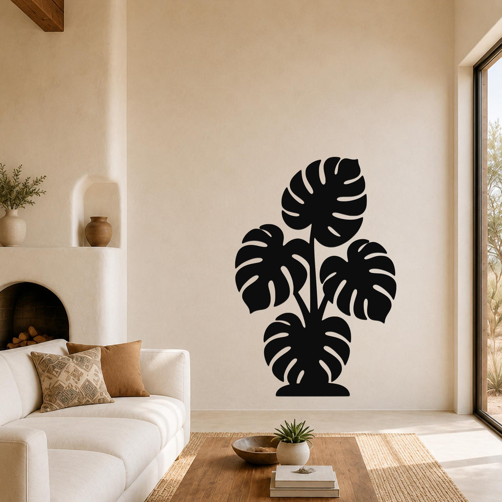 Black metal wall art silhouette of a monstera plant with large leaf cutouts, mounted on a living room wall above a white sofa.