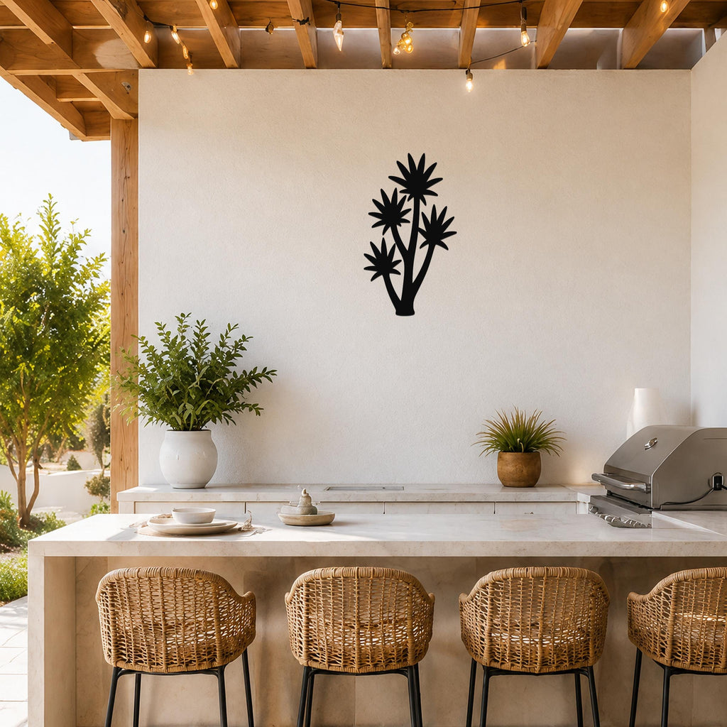 Black metal yucca wall art with layered leaf cutouts, mounted on a white outdoor wall above a kitchen counter.