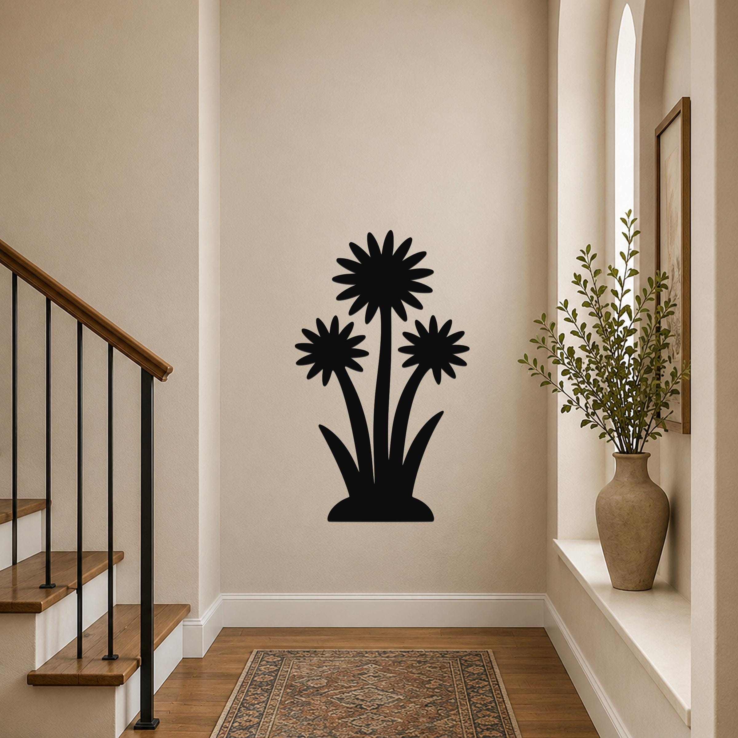 Black metal wall art featuring a silhouette of three wildflowers with layered petals and long stems, mounted on a hallway wall above a patterned rug near a staircase.