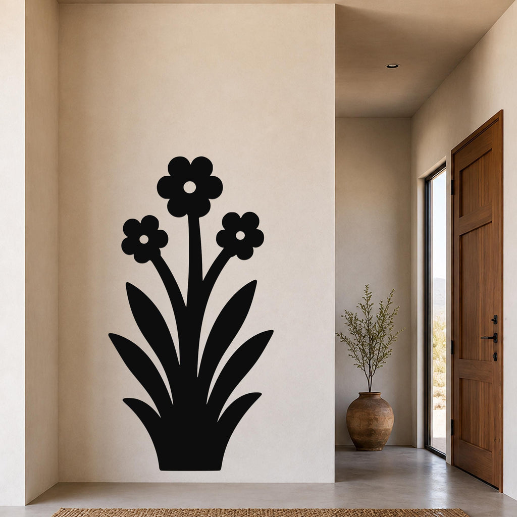 Black metal wall art silhouette of a wildflower with three blooms and long leaves, mounted on a beige wall in a hallway near a wooden door and a potted plant.